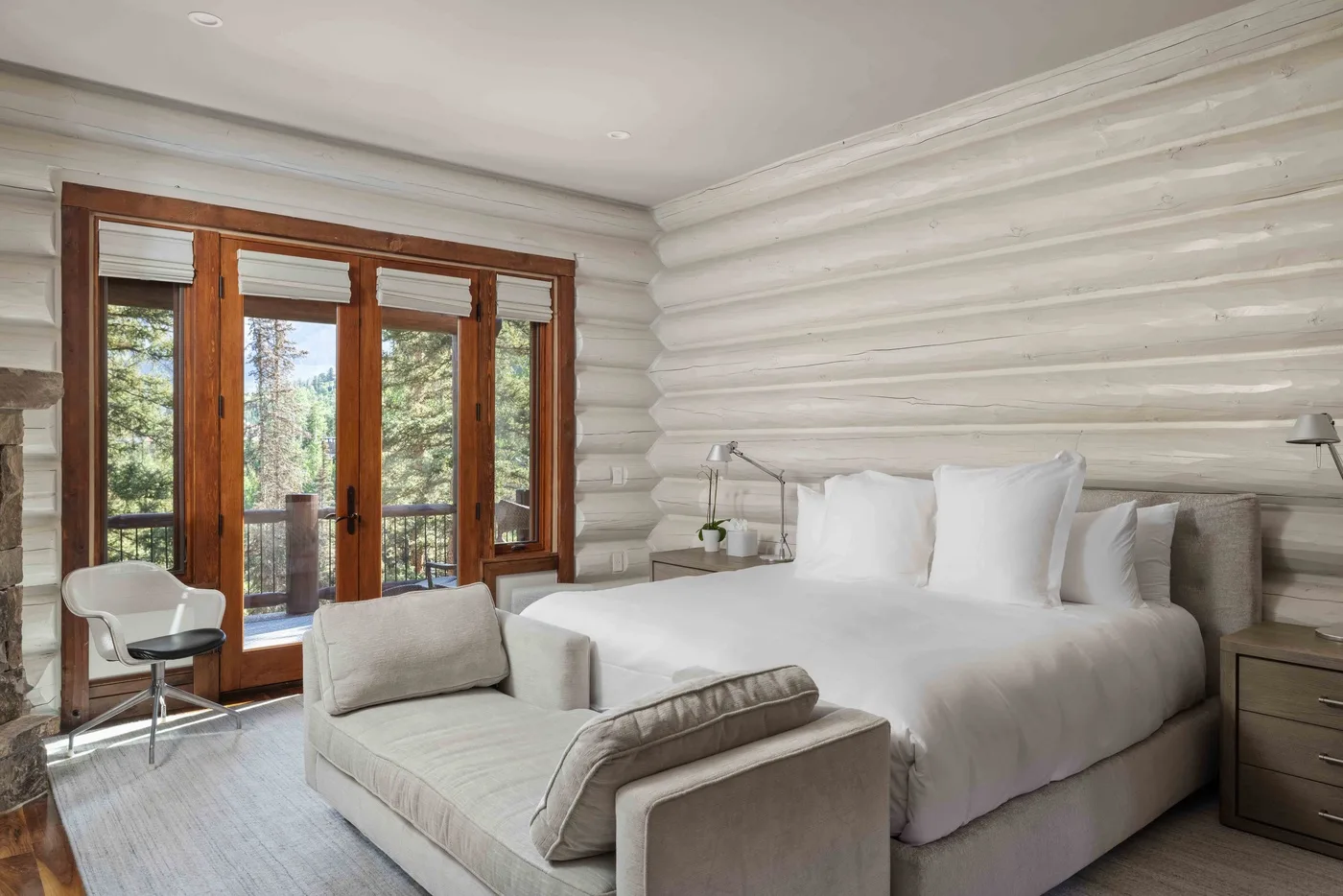 A bedroom with a white bed and seating beside wood-framed glass doors.