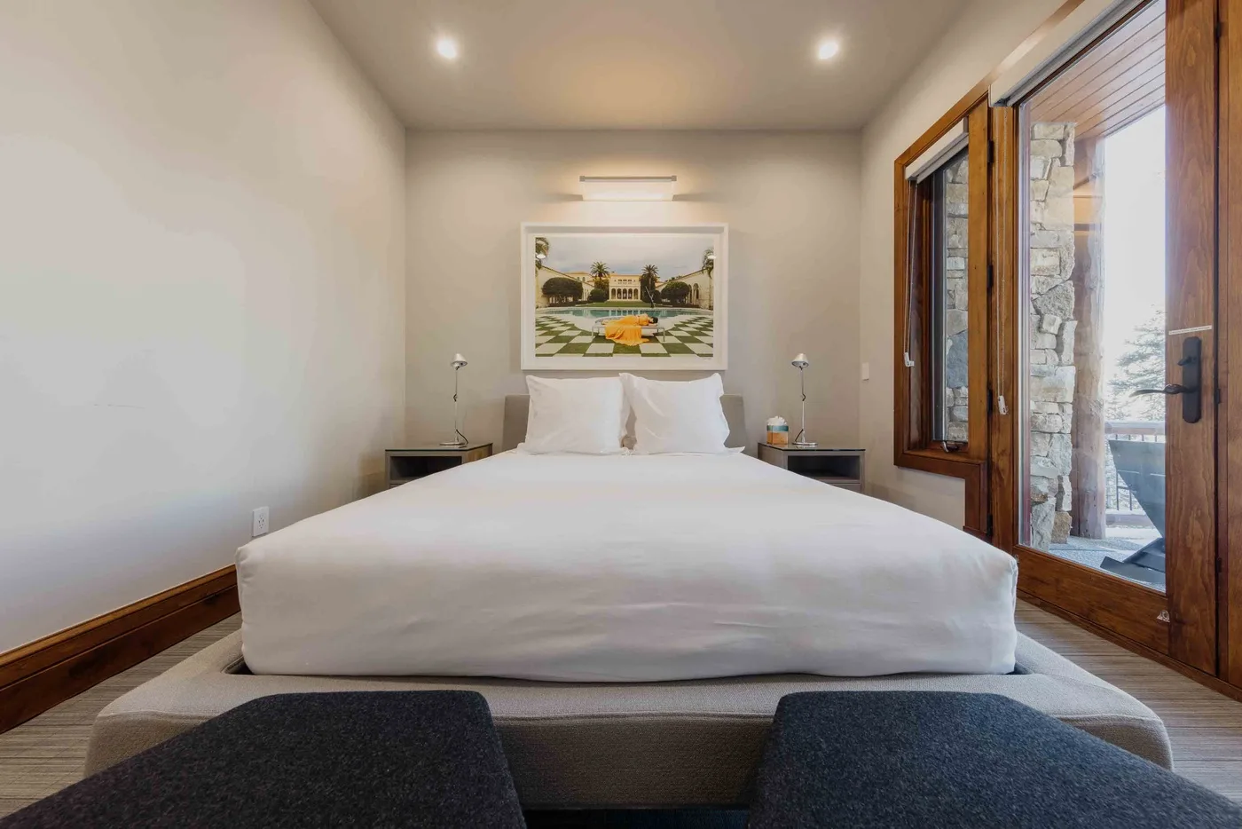 A bedroom with a neatly made bed and large wood-framed windows.