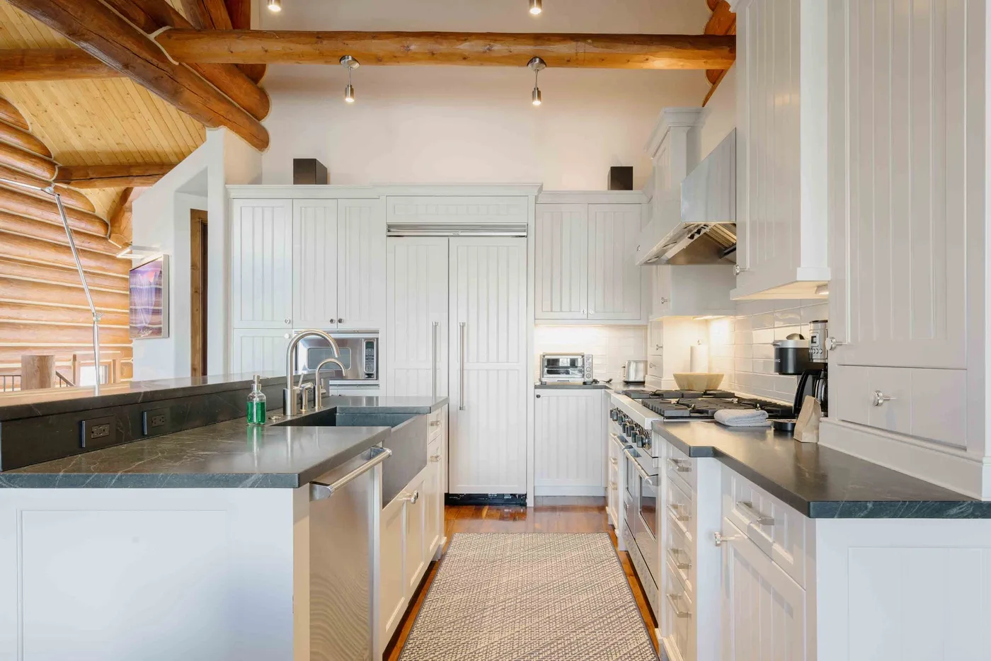 A bright kitchen with white cabinetry, dark countertops, and exposed wooden ceiling beams.