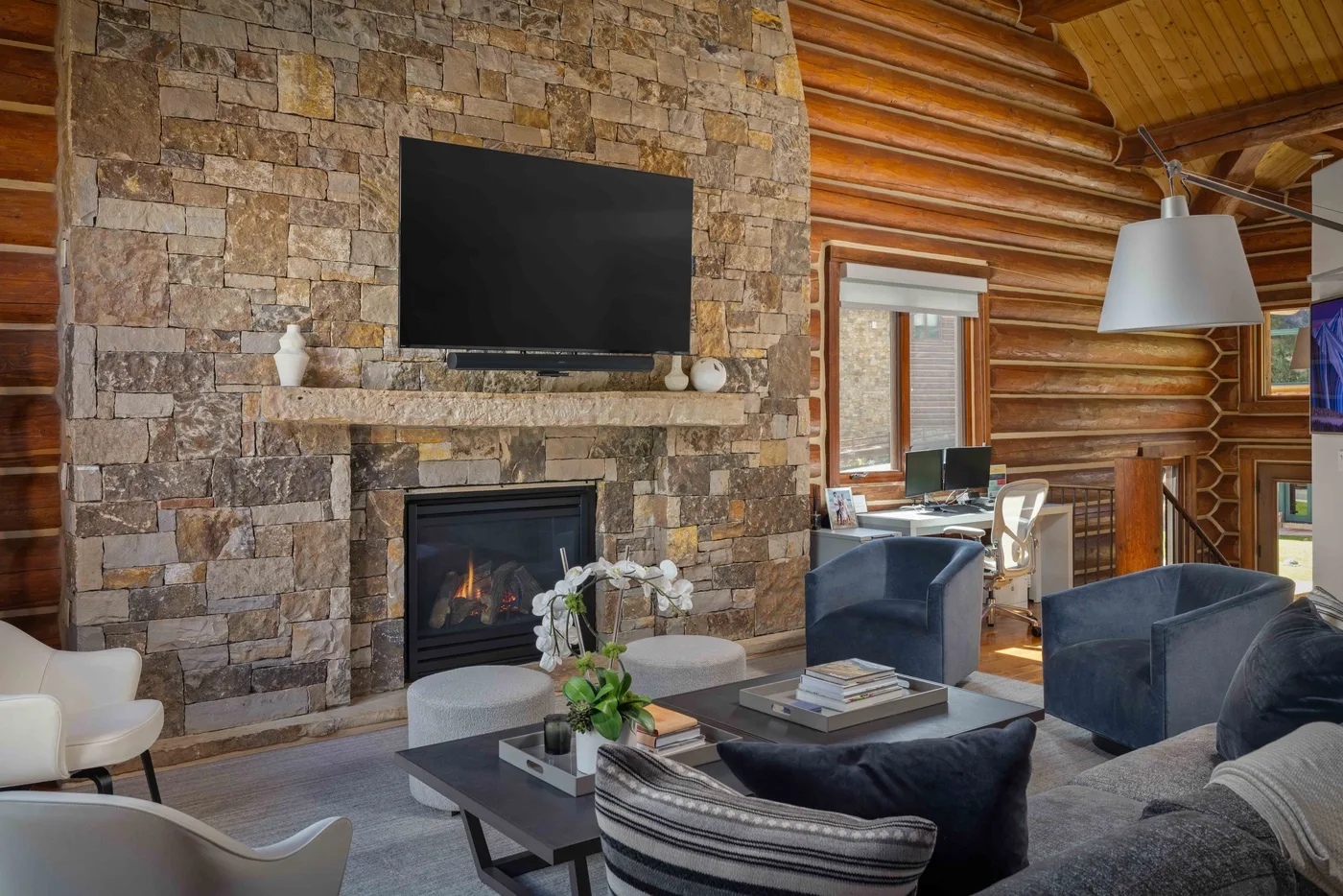 A log-walled living room with a stone fireplace and television.