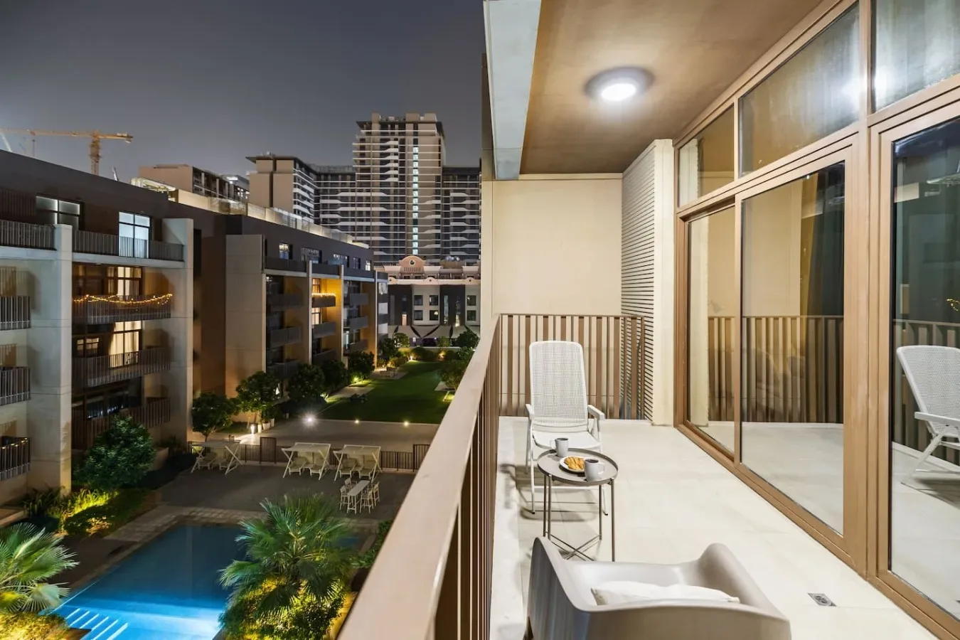 A balcony with seating overlooks a pool and surrounding buildings at night.