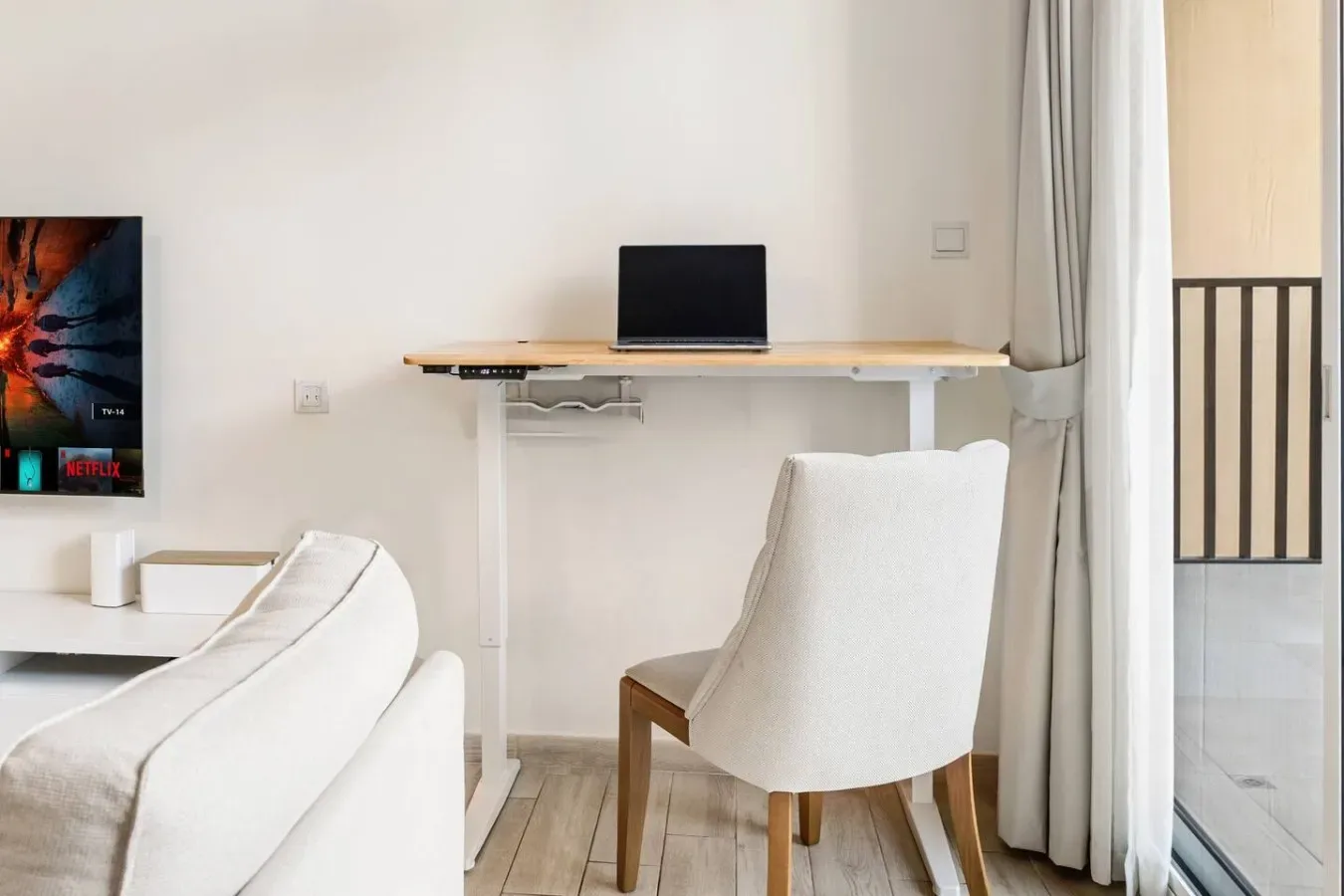 A bright living area with white seating and a desk beneath a window.
