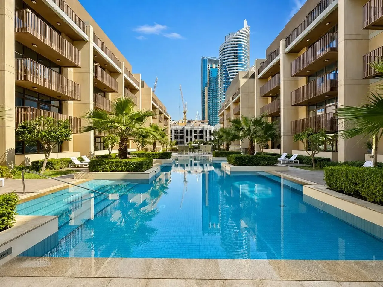Una piscina se encuentra entre edificios modernos, con palmeras junto al borde.