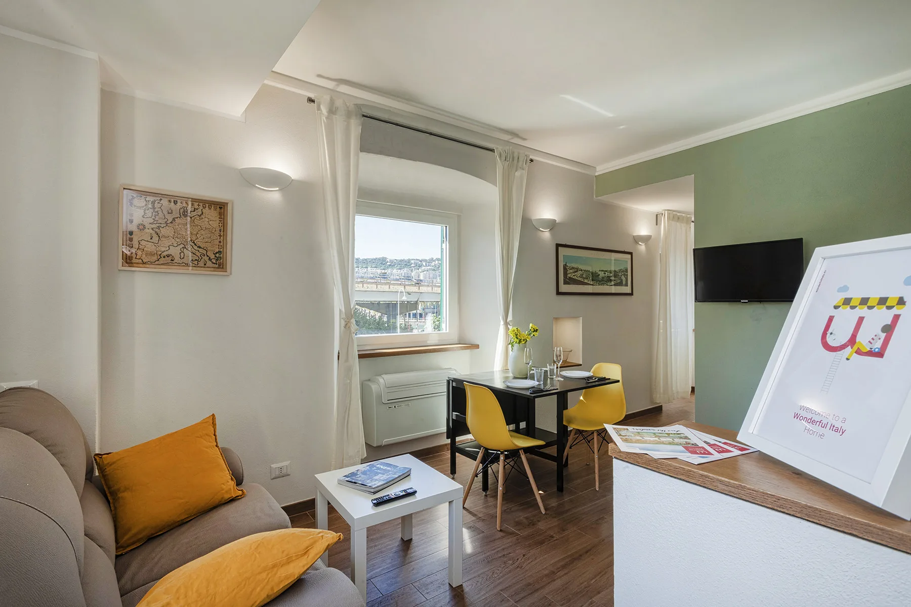 A bright living area with a sofa, small dining table, and wall-mounted television.