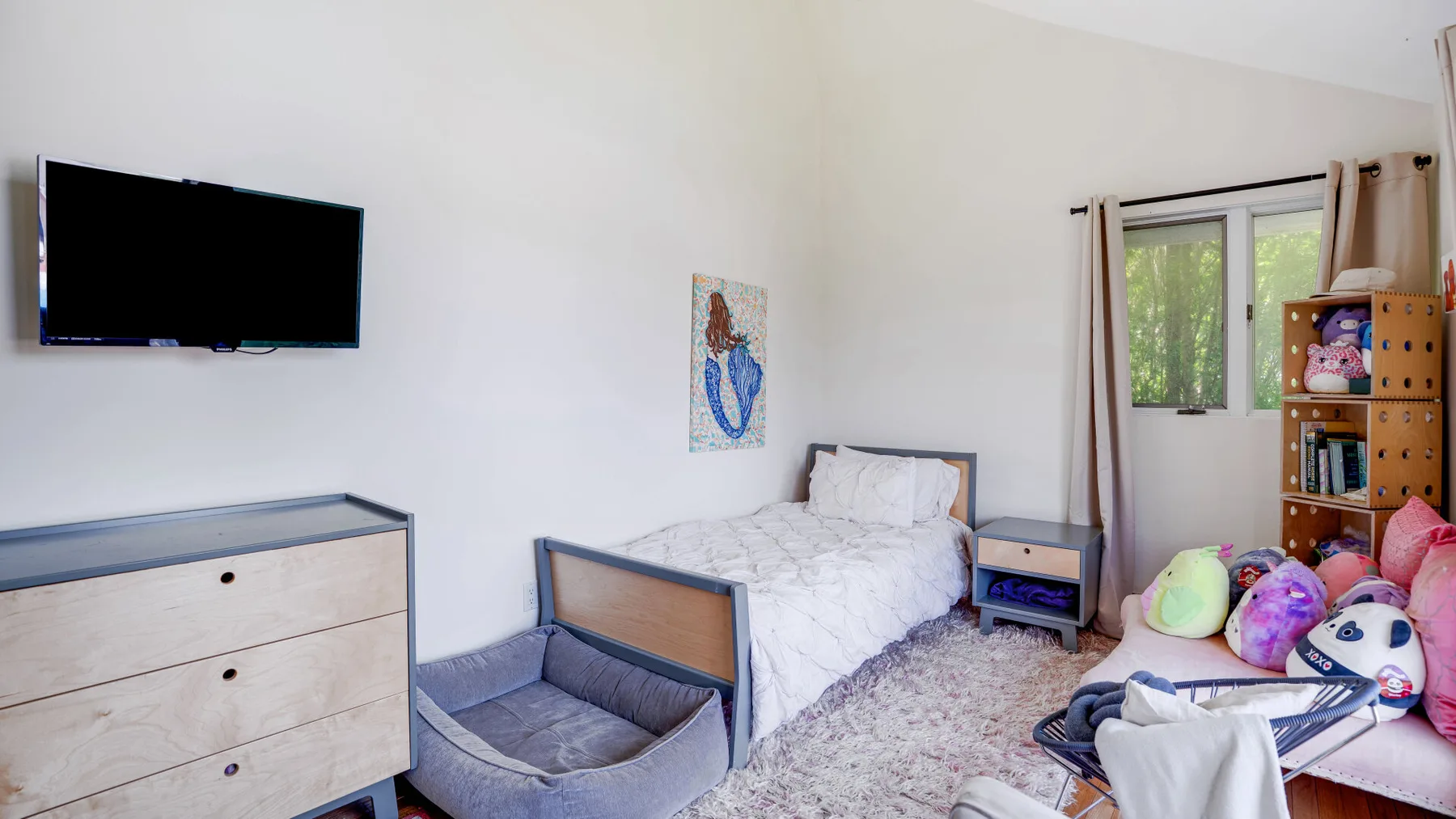 A bedroom with a single bed, television, dresser, and window.