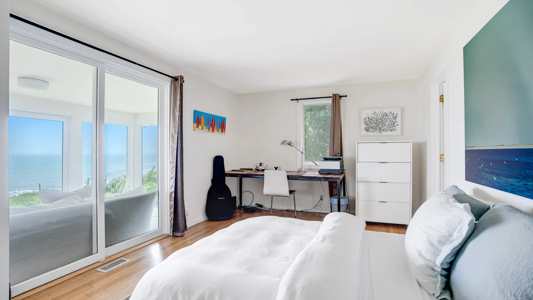 A bright bedroom with a bed, desk, and sliding glass doors overlooking the water.