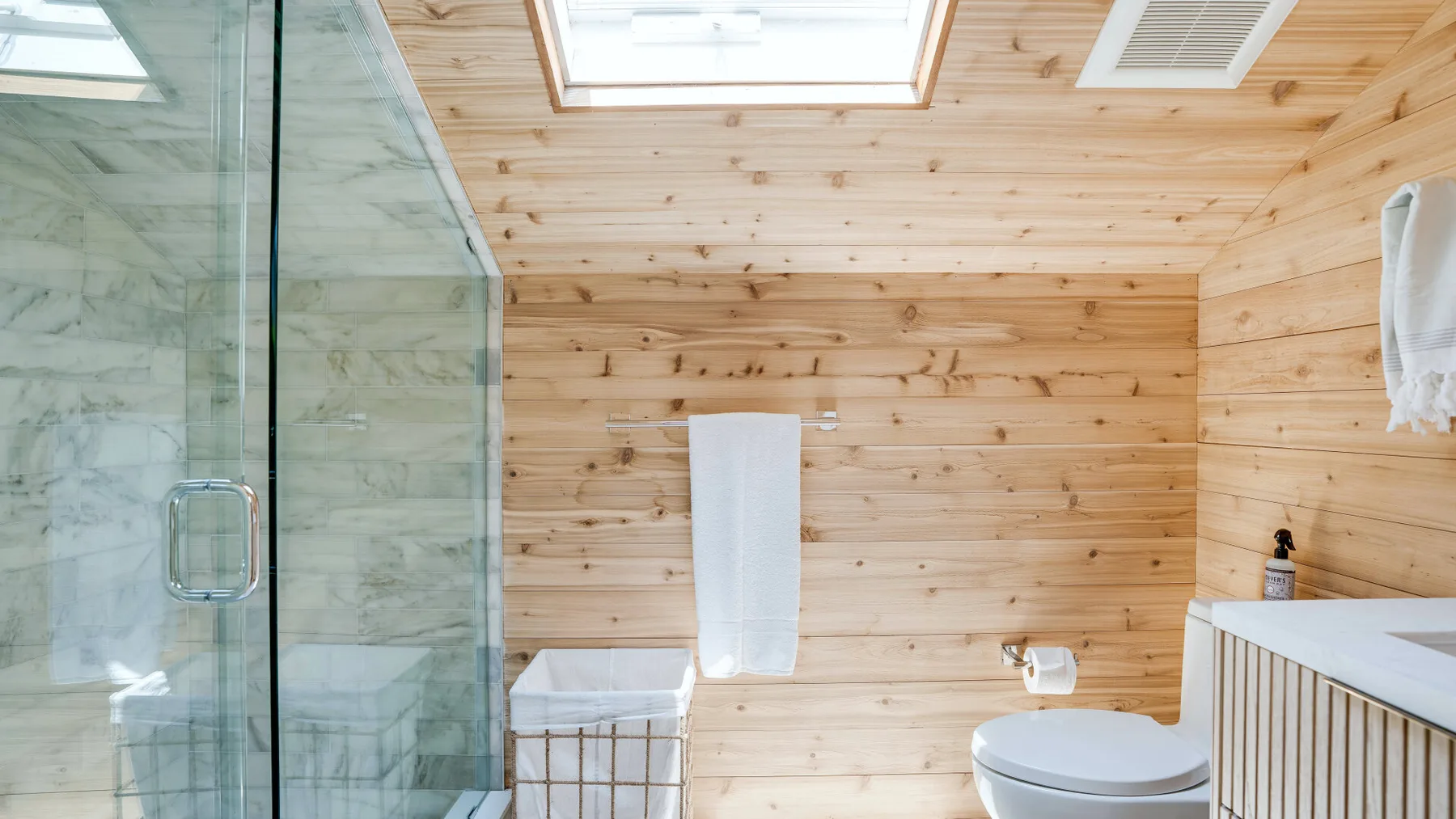 A bathroom with a glass shower and wood-paneled walls.