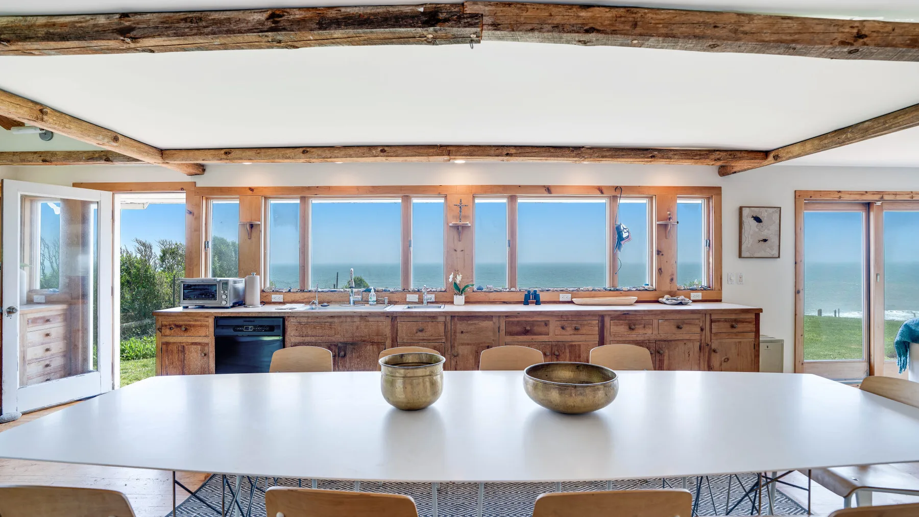 A bright dining area with a broad table and large windows overlooking the sea.