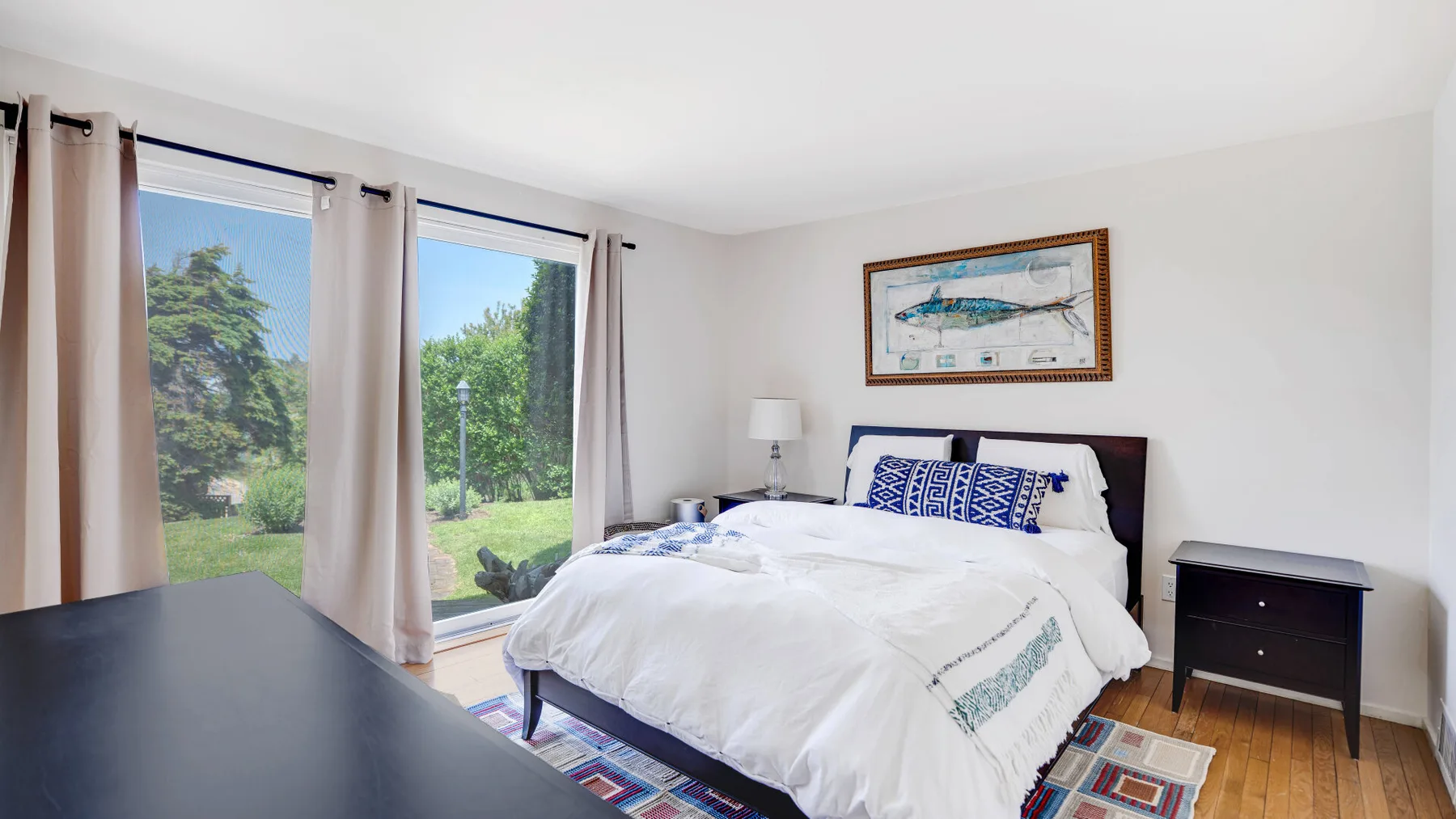 A bedroom with a neatly made bed beside large windows overlooking greenery.