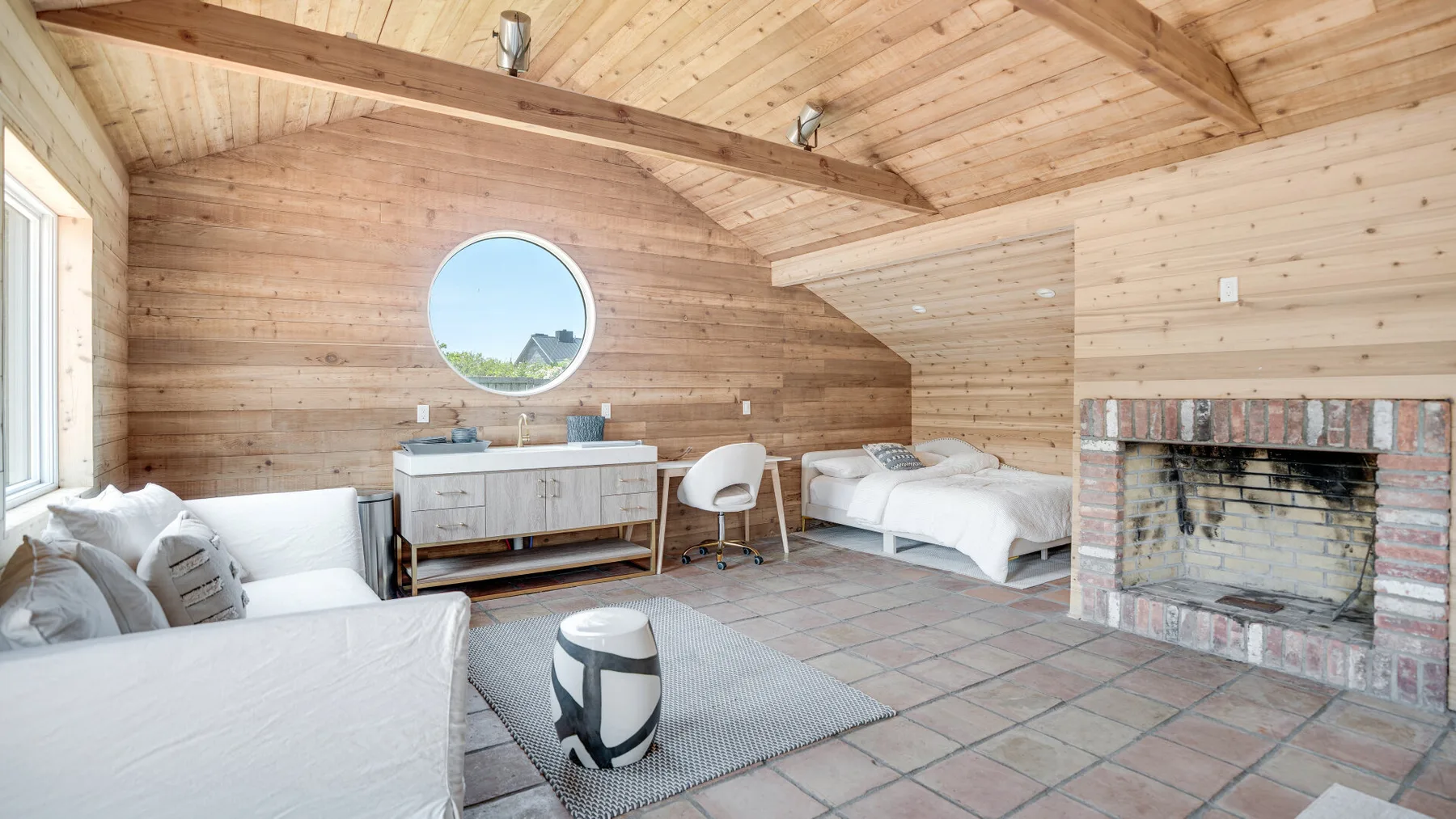 A wood-paneled bedroom with beds, seating, and a brick fireplace.
