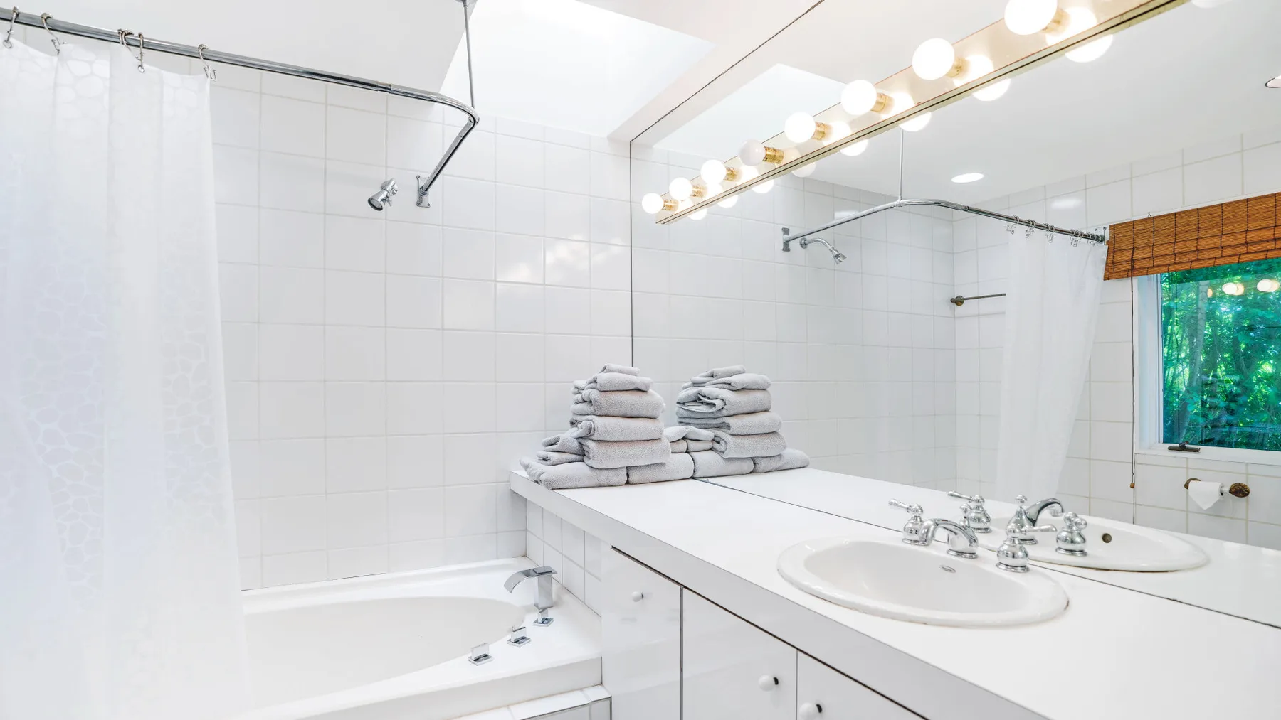 A bright bathroom with a bathtub, shower curtain, and long vanity.