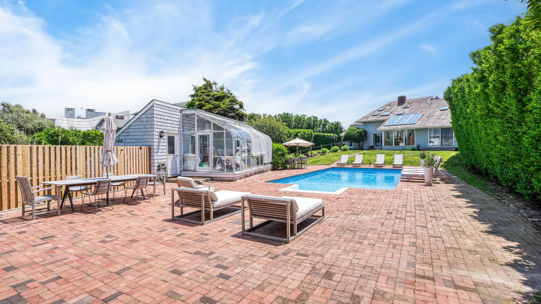 A sunny outdoor pool area with brick paving, loungers, and a glass-enclosed structure.