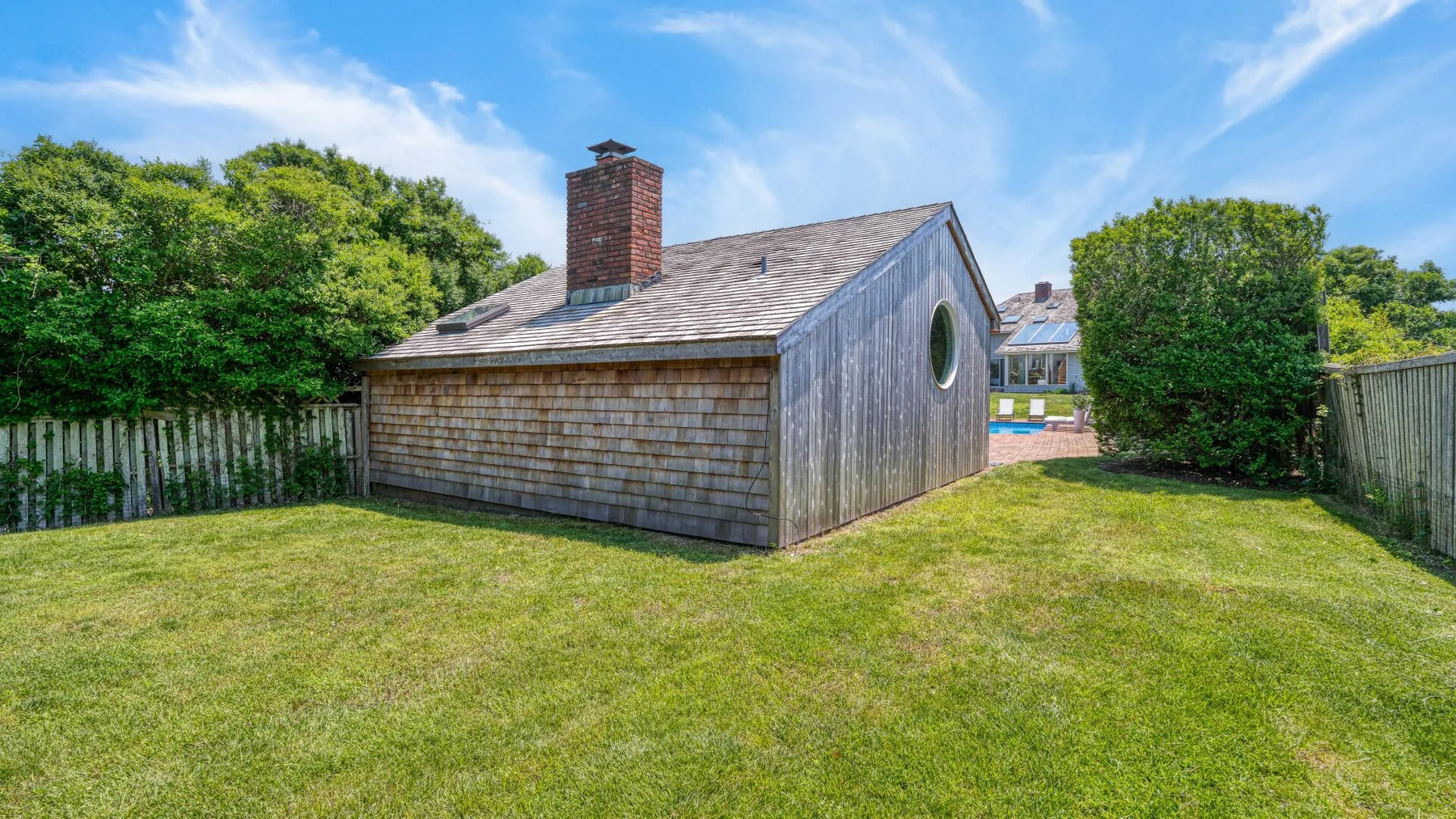 A small shingled building stands in a grassy yard among trees.
