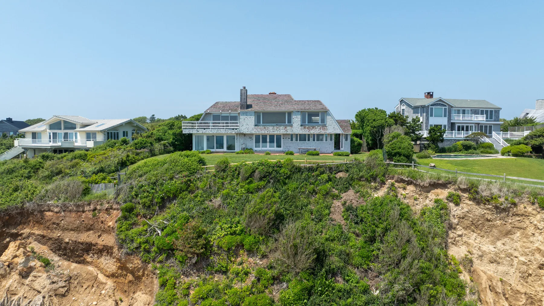 Houses stand along a coastal bluff above exposed earth and vegetation.