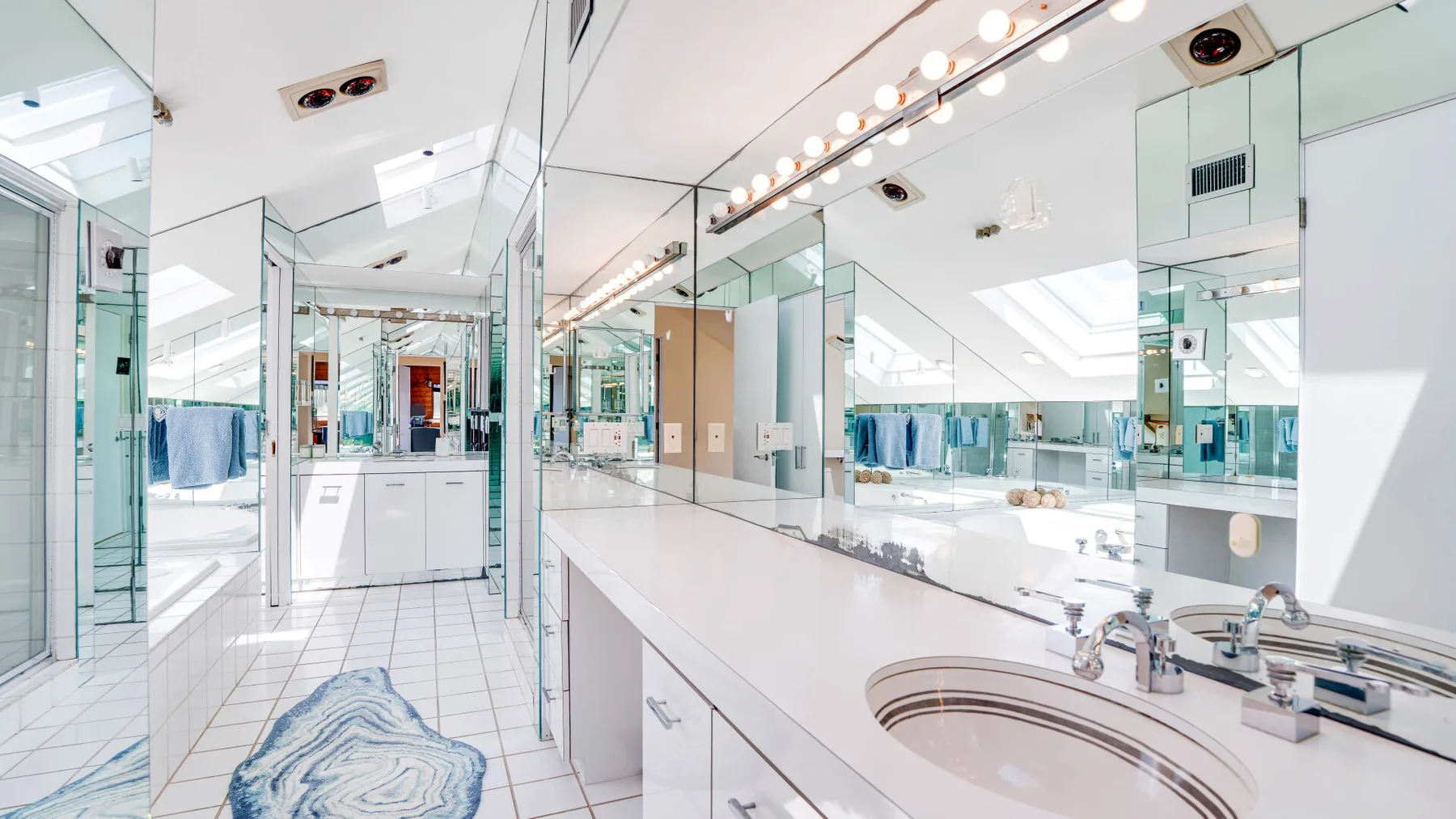 A bright bathroom with mirrored walls, a long counter, and an oval sink.