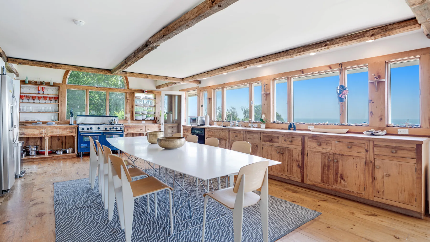 A bright kitchen and dining area with a long table beside large windows.