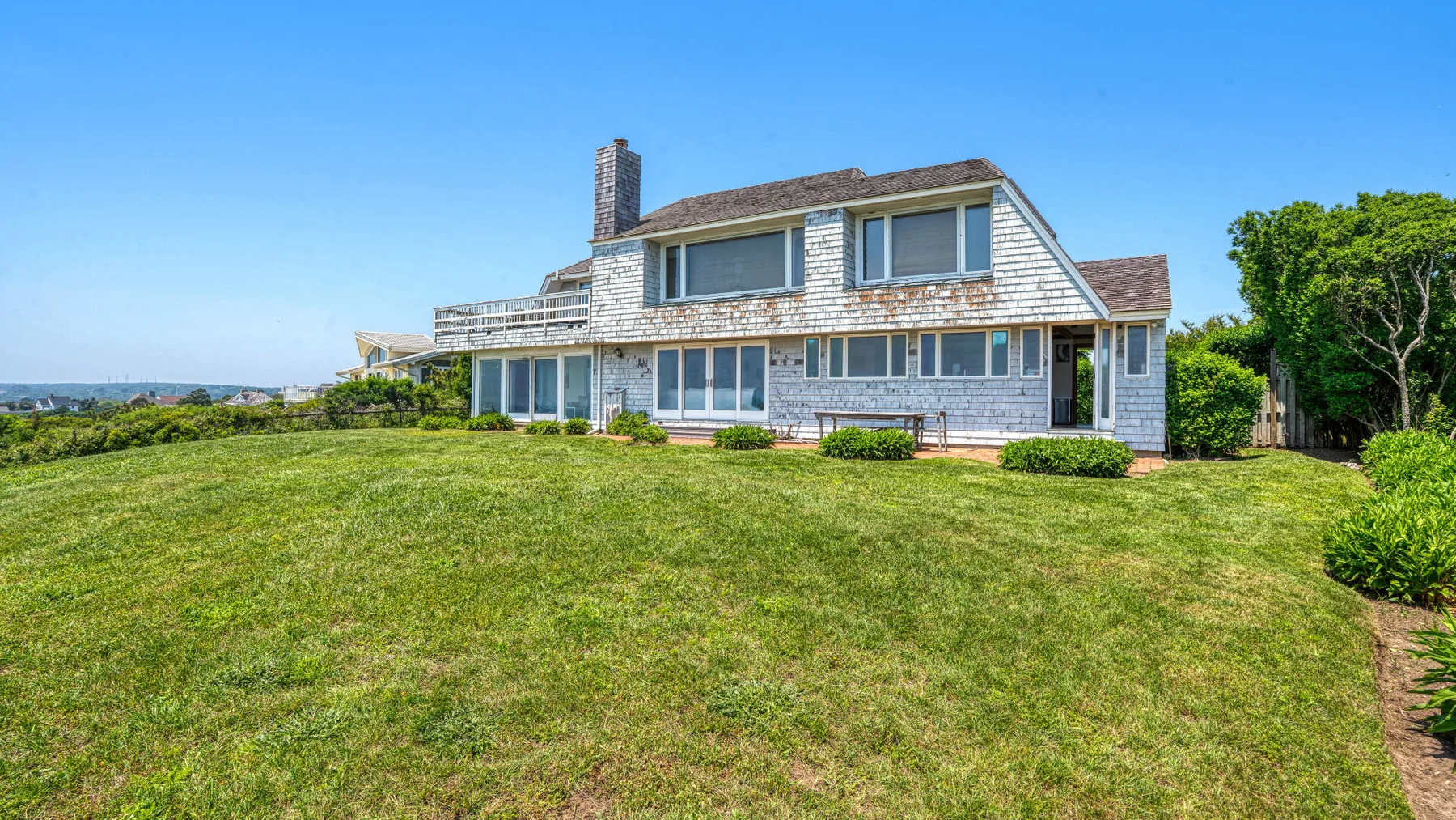 A large house stands behind a broad green lawn beneath a clear blue sky.