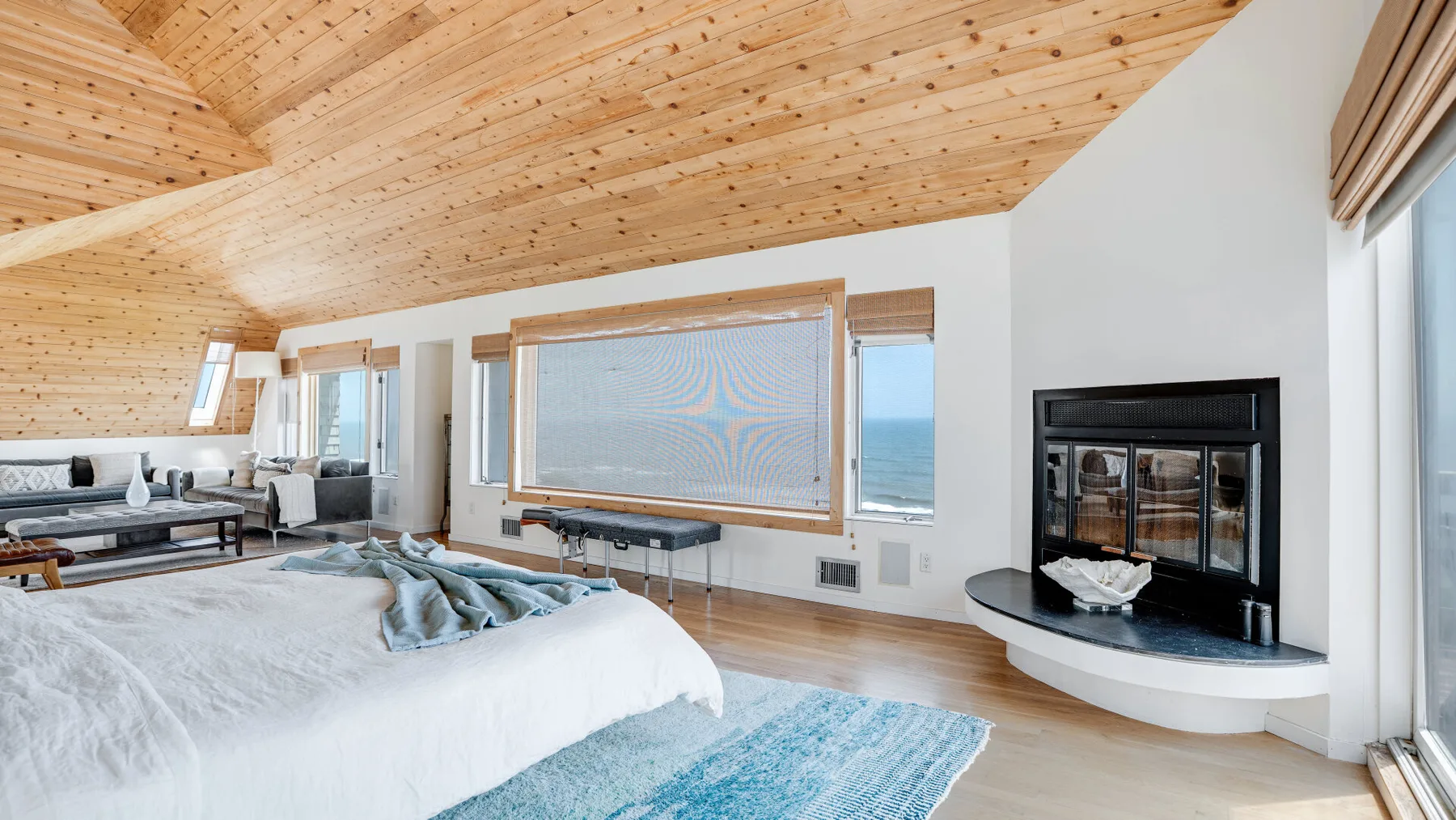 A bright bedroom with a sloped wooden ceiling and a bed beside a fireplace.