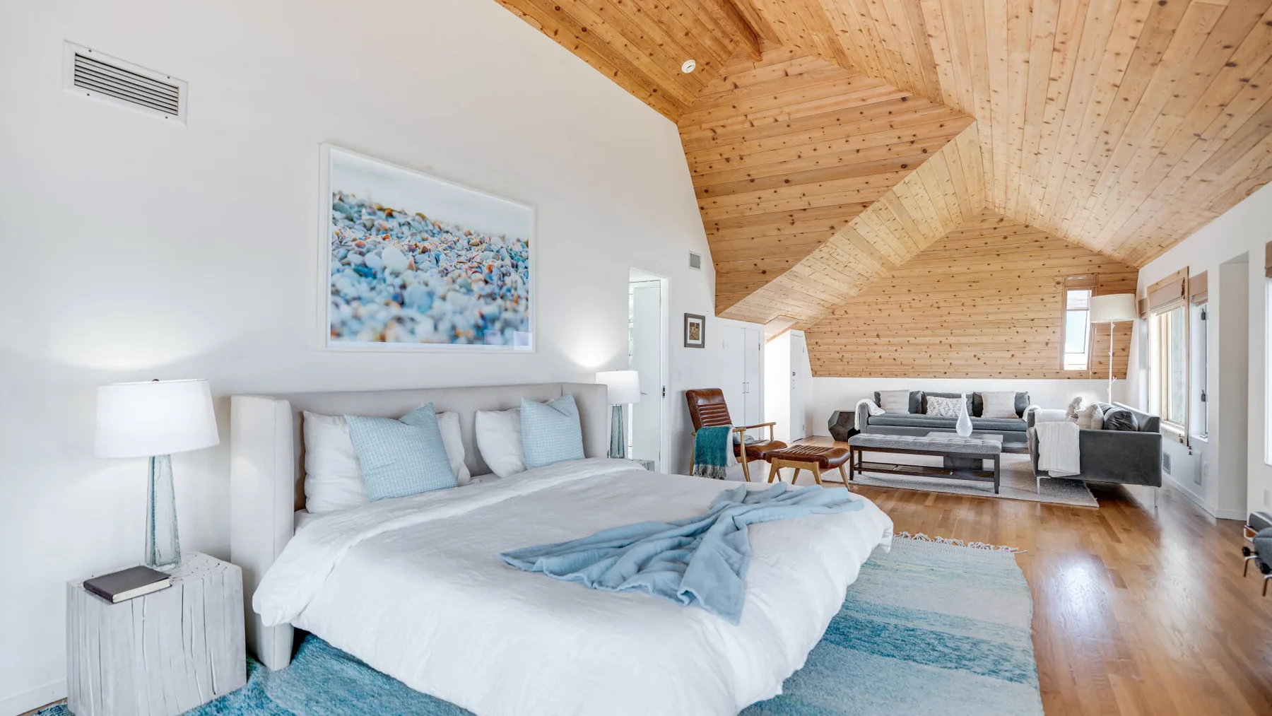 A bright bedroom with a large bed beneath a sloped wooden ceiling.