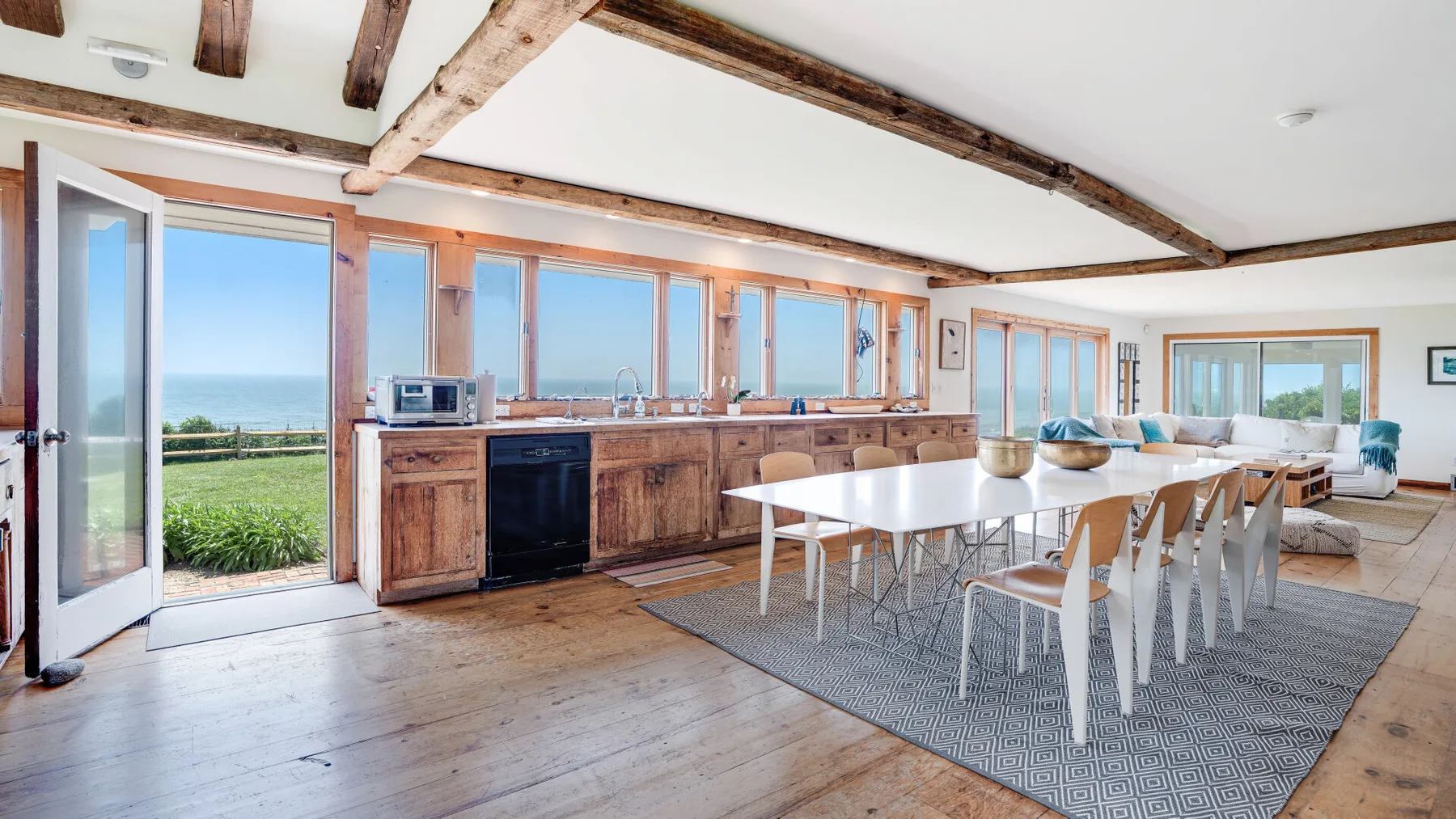 A bright dining room with a long table beside large windows overlooking the landscape.
