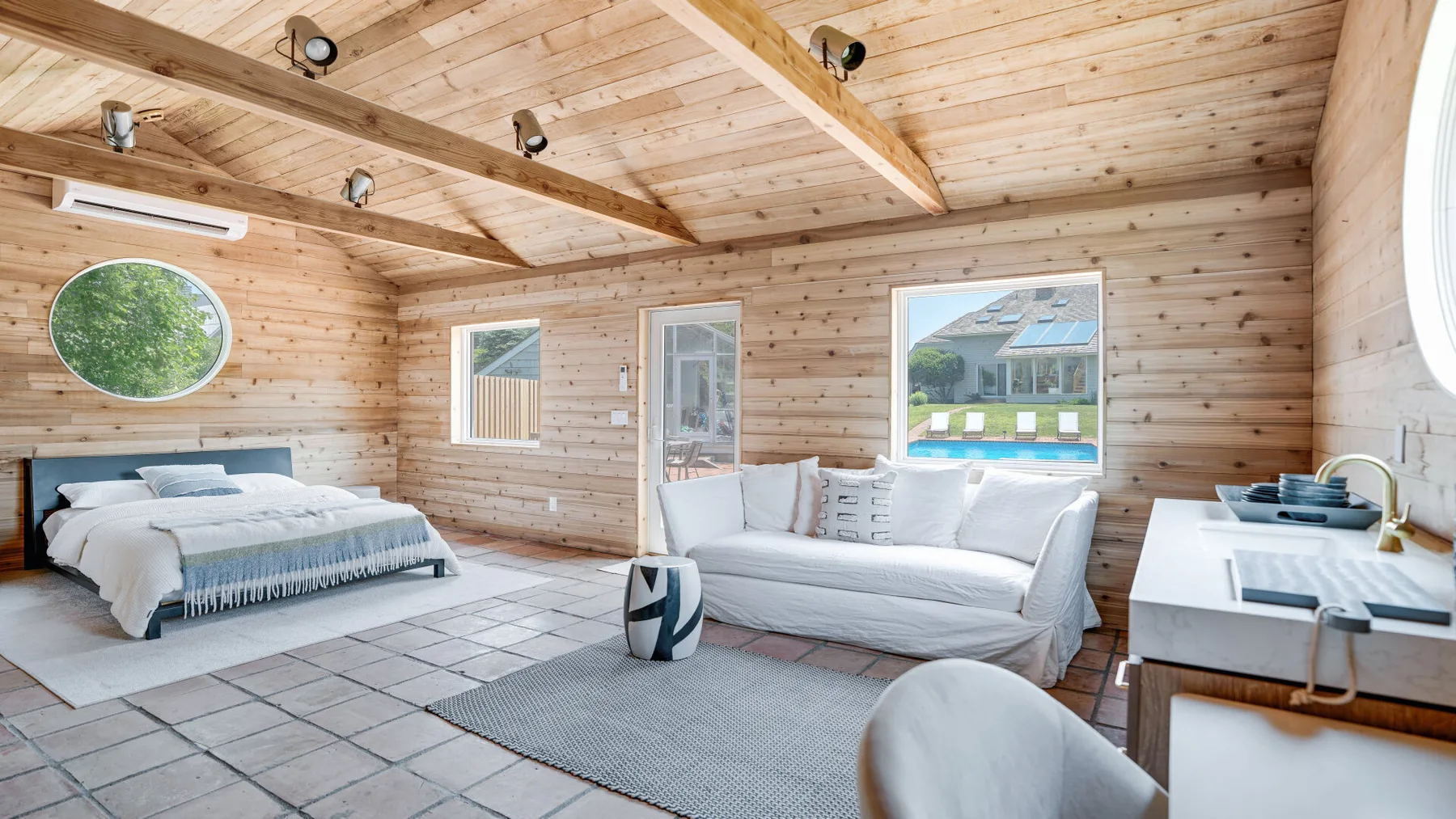A bright wood-paneled bedroom with a bed, seating area, and kitchenette.