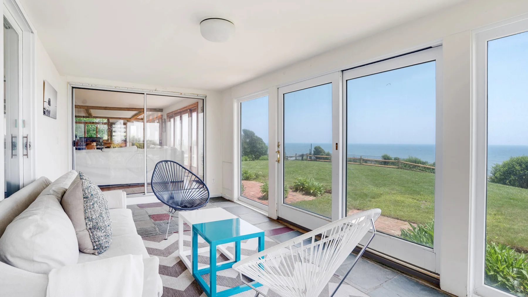 A bright living room with large windows overlooking a green lawn and the sea.