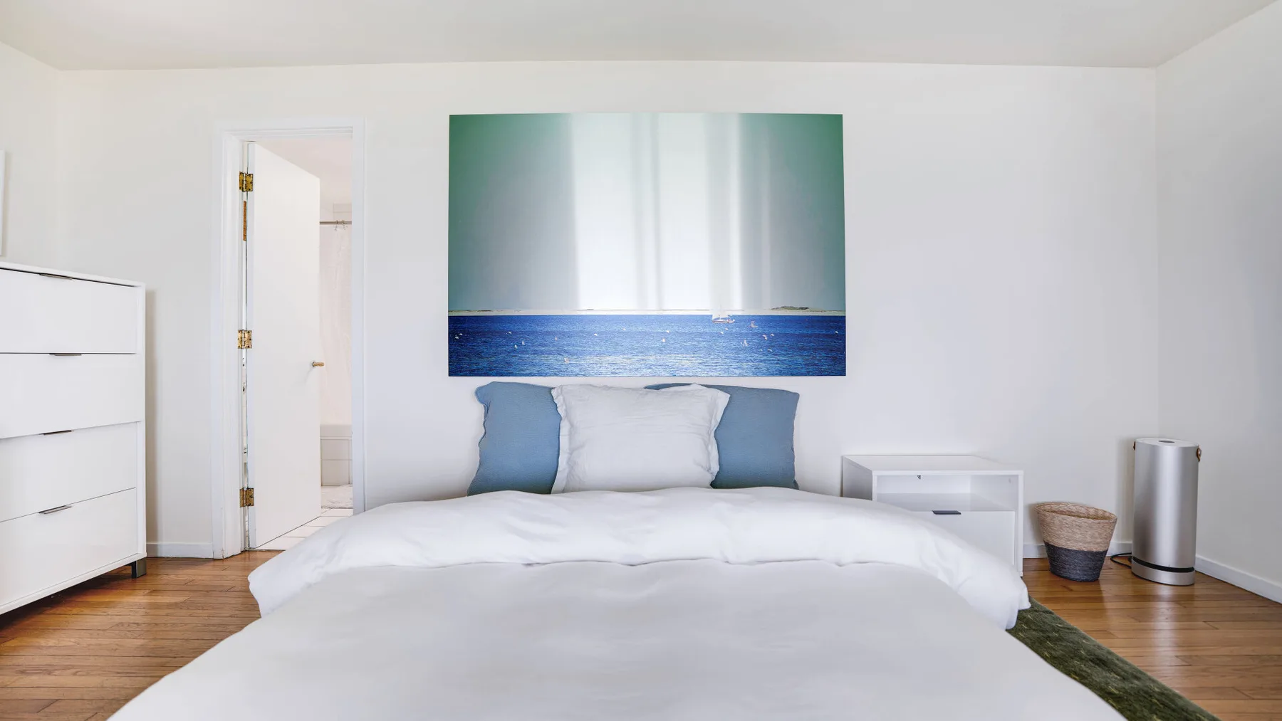 A bedroom with a bed beneath a large ocean-themed wall picture.
