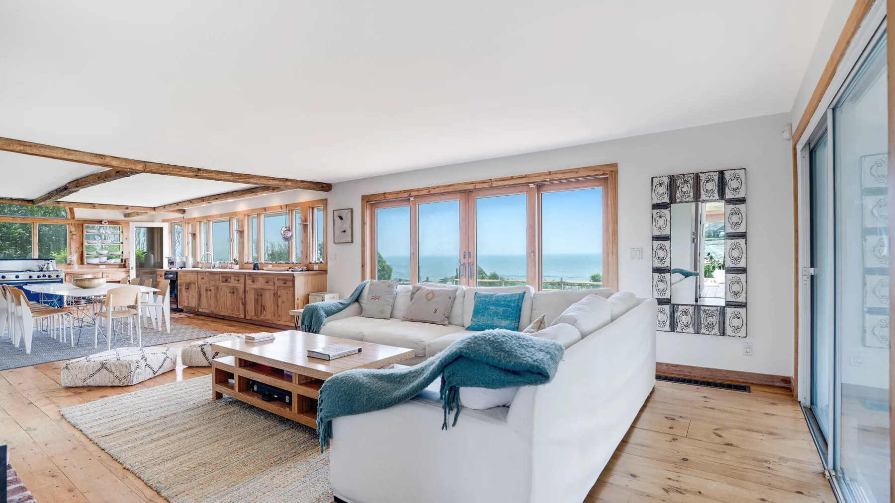 A bright living room with a white seating area facing large windows overlooking the sea.