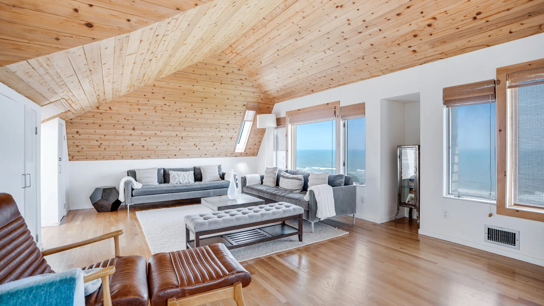 A bright living room with seating, large windows, and a sloped wood ceiling.