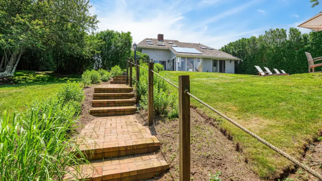 A house overlooks a grassy yard with brick steps and a simple rail.