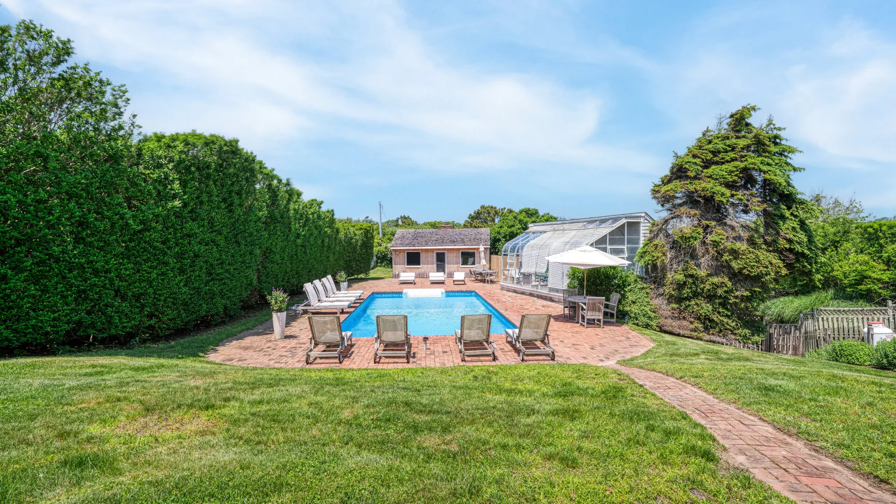 Outdoor pool area with lounge seating, greenery, and a paved path.