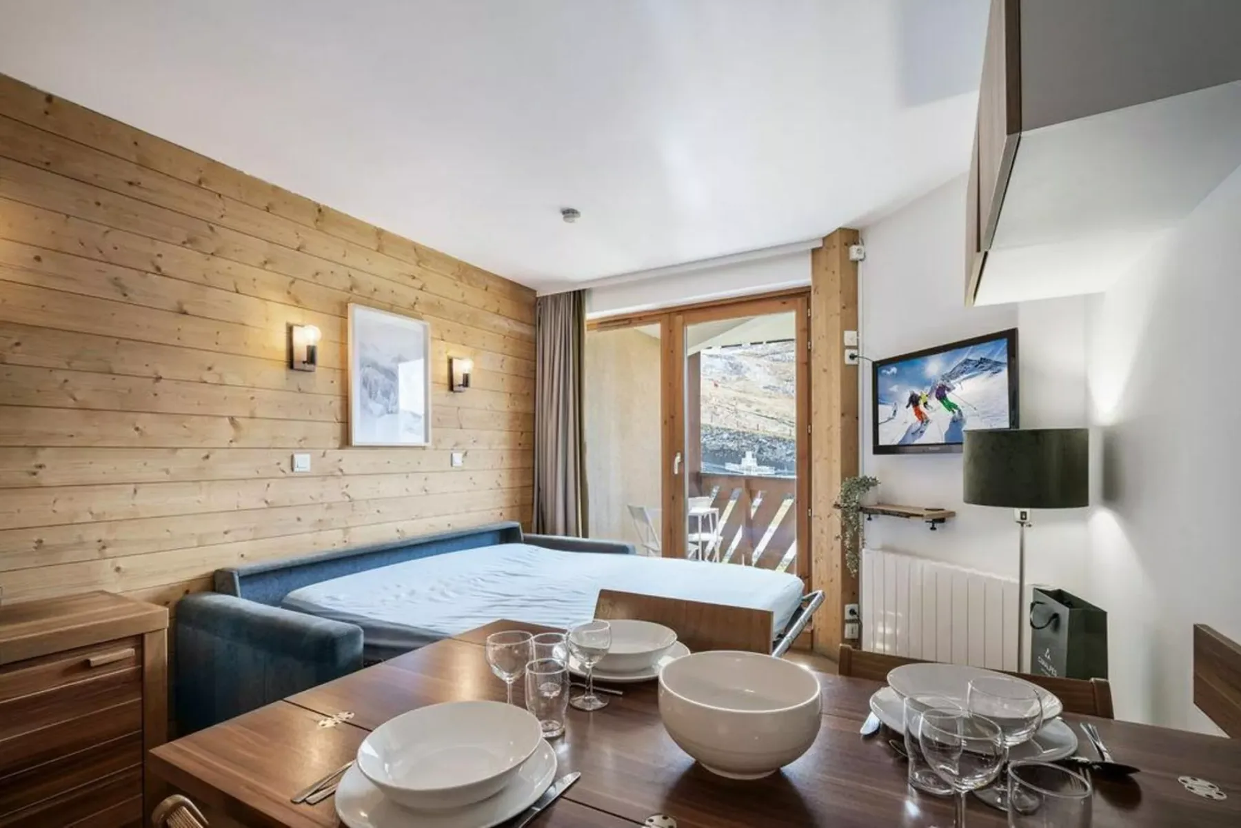 Una mesa de comedor y asientos están junto a una cama en una habitación luminosa.