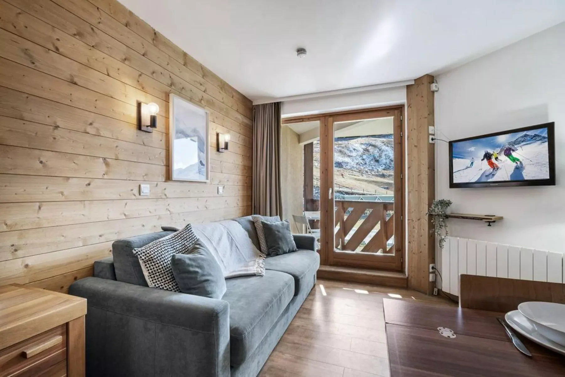 Una sala de estar con un sofá gris y una puerta de vidrio con vistas a las montañas.