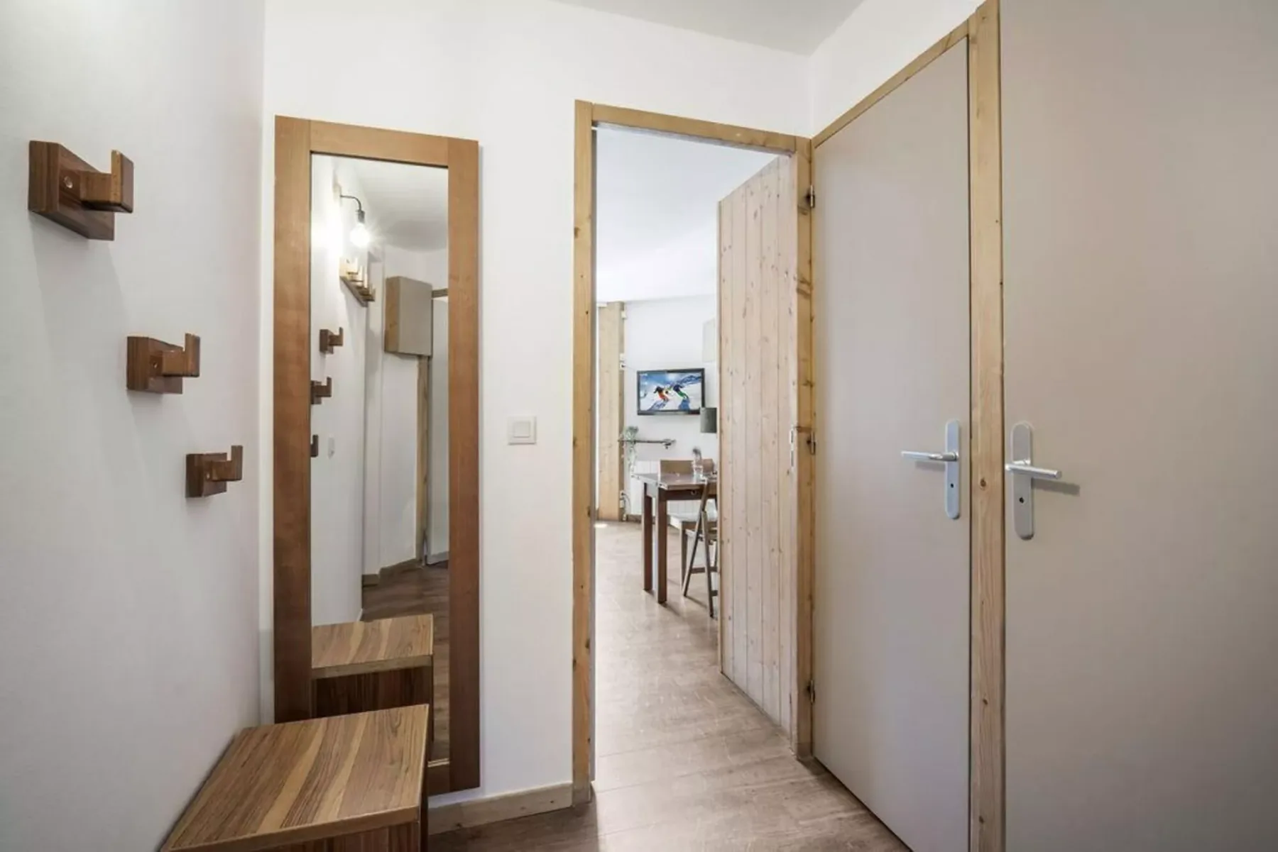Un pasillo luminoso con un espejo de cuerpo entero y una puerta abierta hacia un comedor.