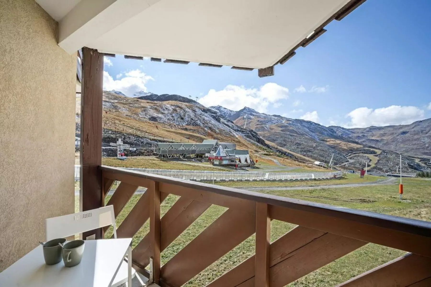 Un balcón cubierto da a un paisaje montañoso, con una mesa pequeña y asientos.