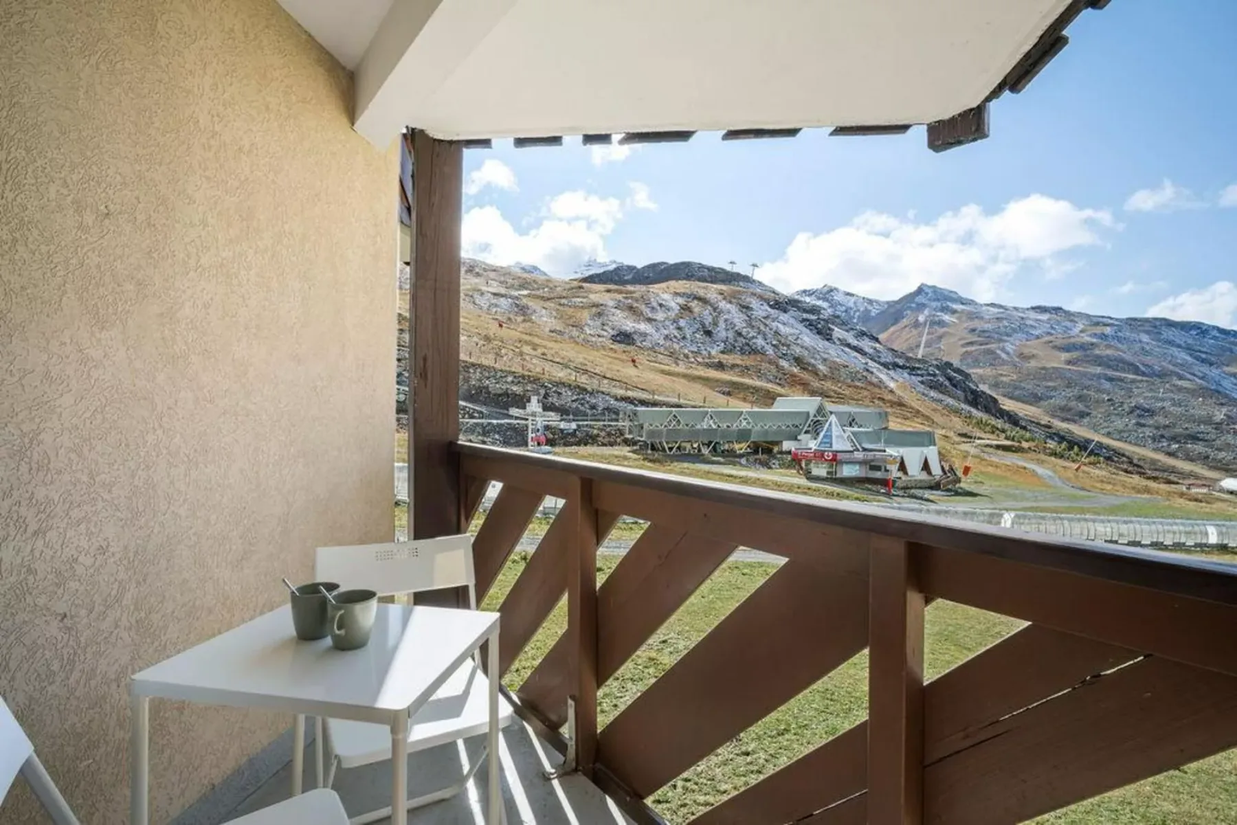 Una zona de estar en un balcón da a un paisaje montañoso y edificios cercanos.