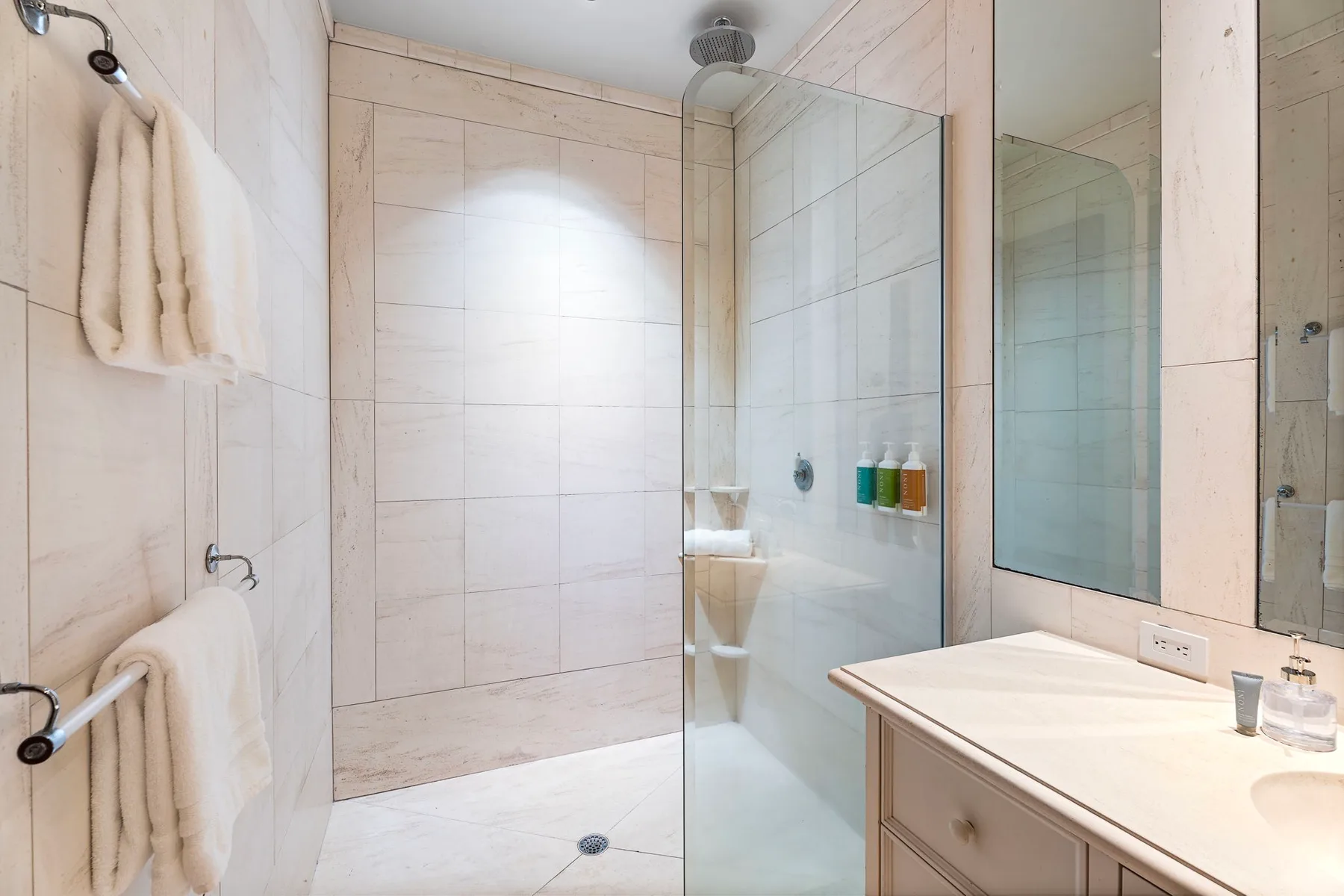 A tiled bathroom with a glass shower, wall mirror, and sink vanity.
