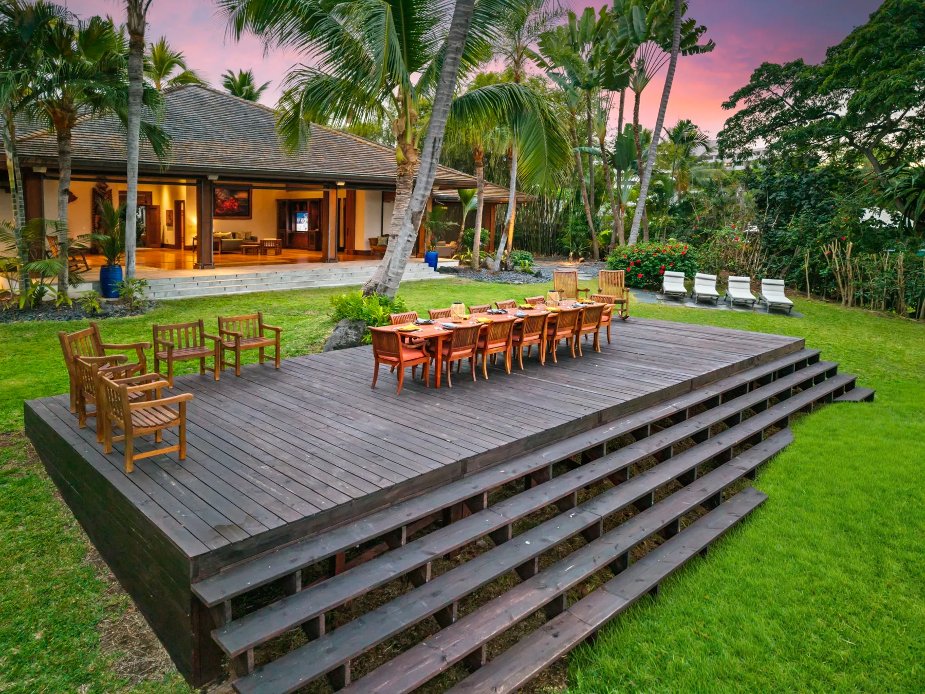 A spacious outdoor dining deck with a long wooden table and surrounding tropical greenery.