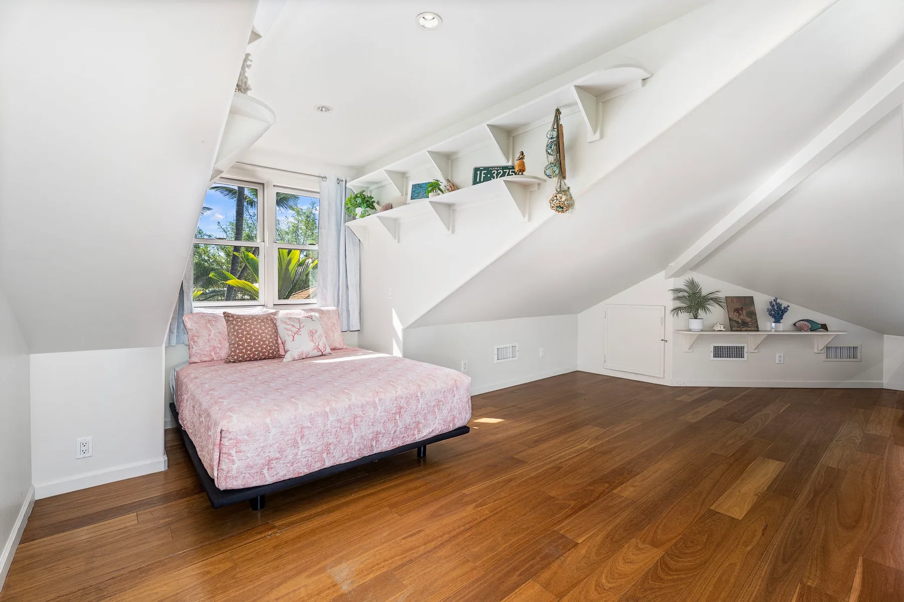 A bright attic bedroom with a bed beneath a sloped ceiling and wood flooring.