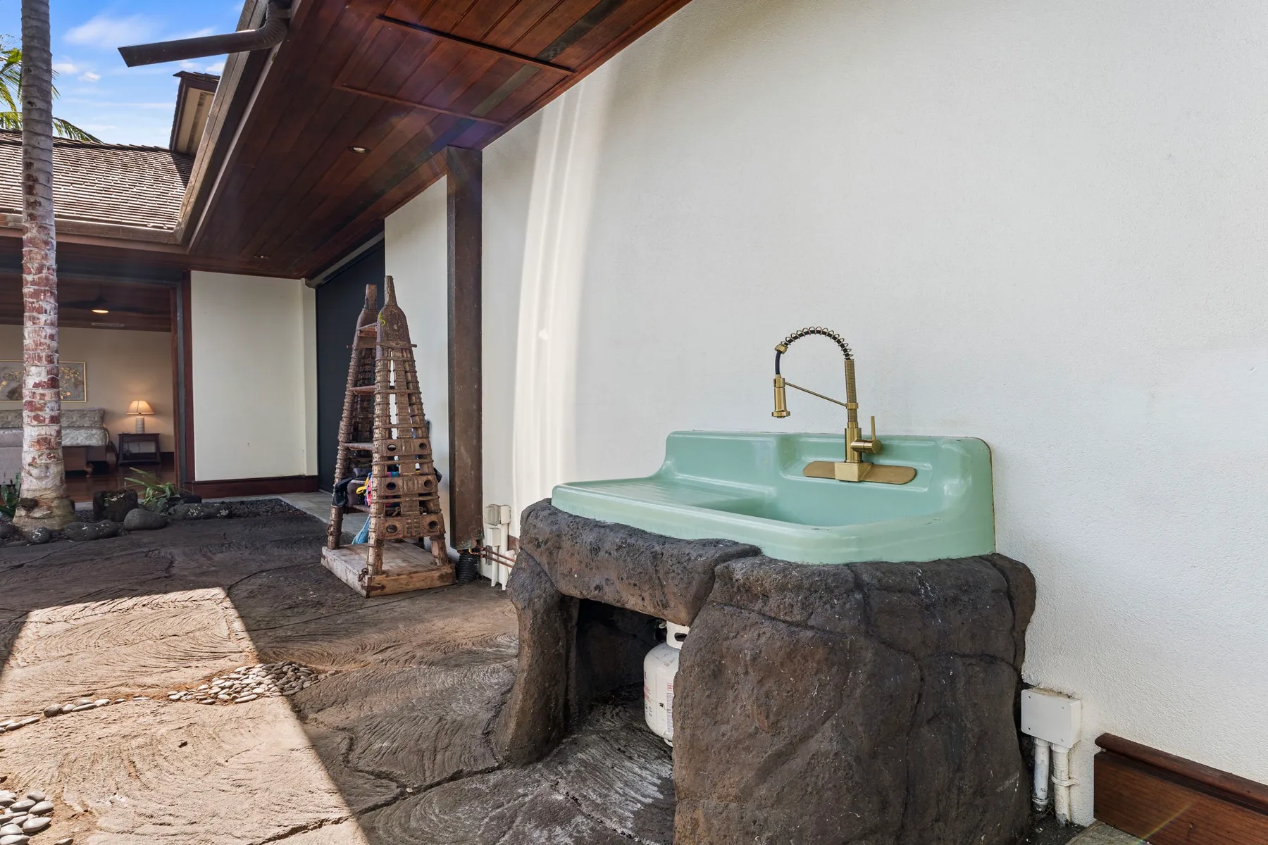 An outdoor washbasin with a brass faucet stands beside a white wall.