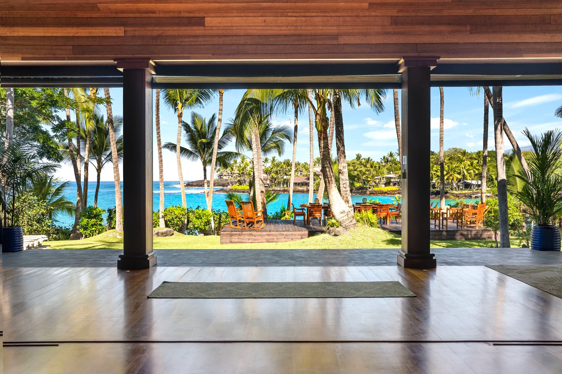 An open-air pavilion overlooks palm trees, outdoor seating, and the ocean.