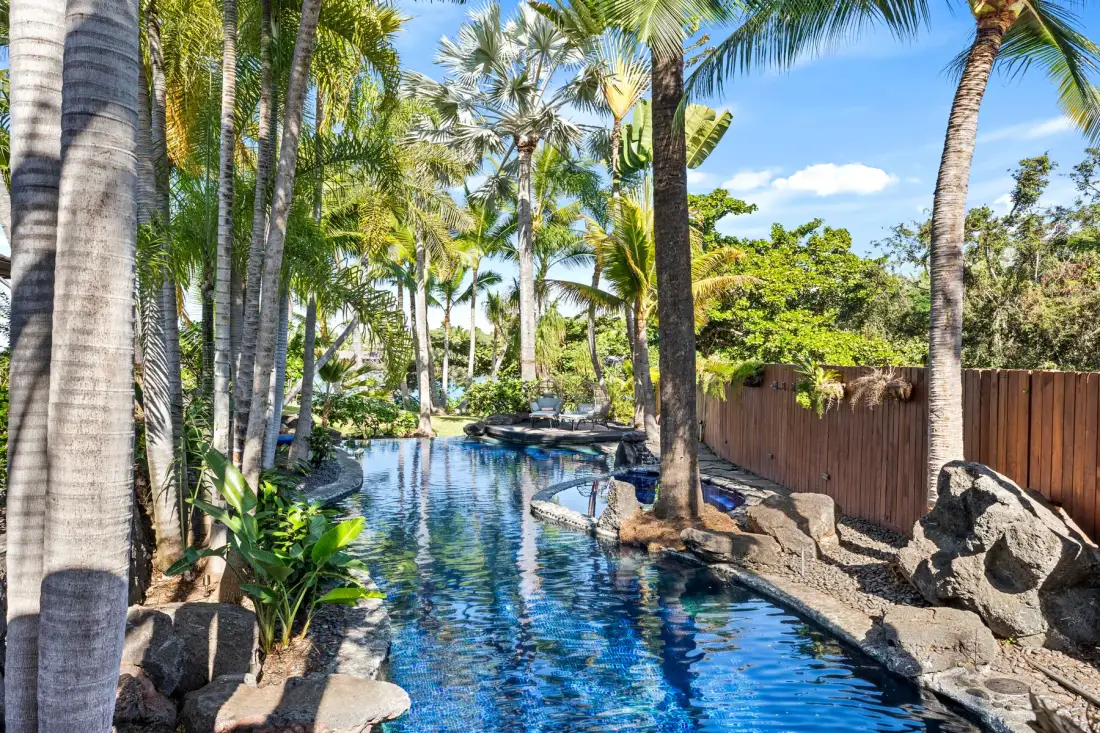 A swimming pool winds through a tropical garden lined with palm trees.