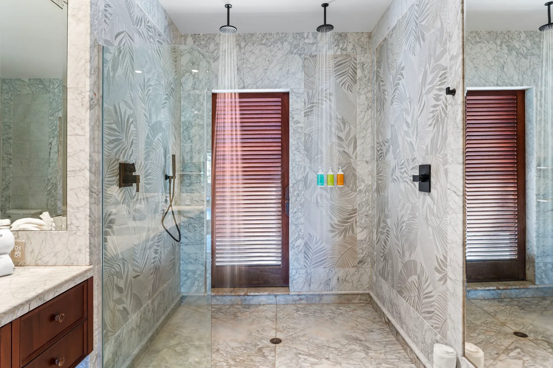 A tiled bathroom with a glass shower and a window with blinds.