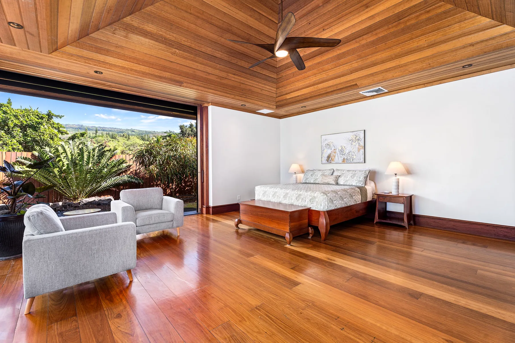 A bedroom with a bed, seating, and a wide opening to a garden.