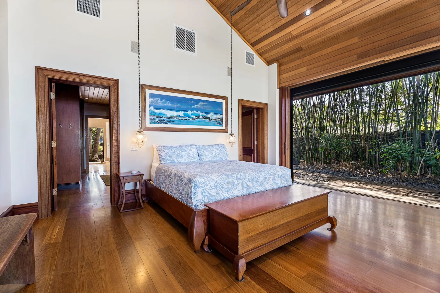 A bedroom with a bed beneath a wood-paneled ceiling and a garden view.