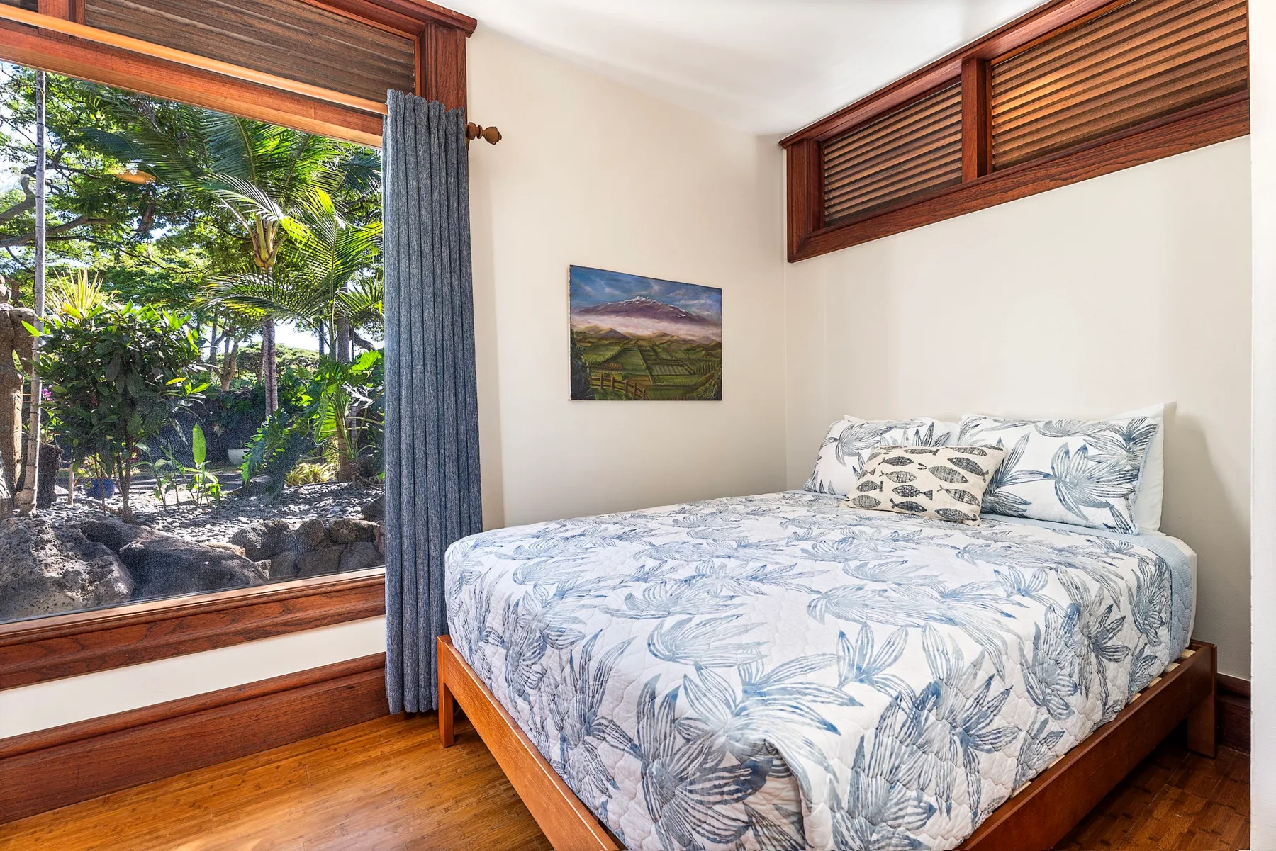 A bedroom with a bed beside a large window overlooking greenery.