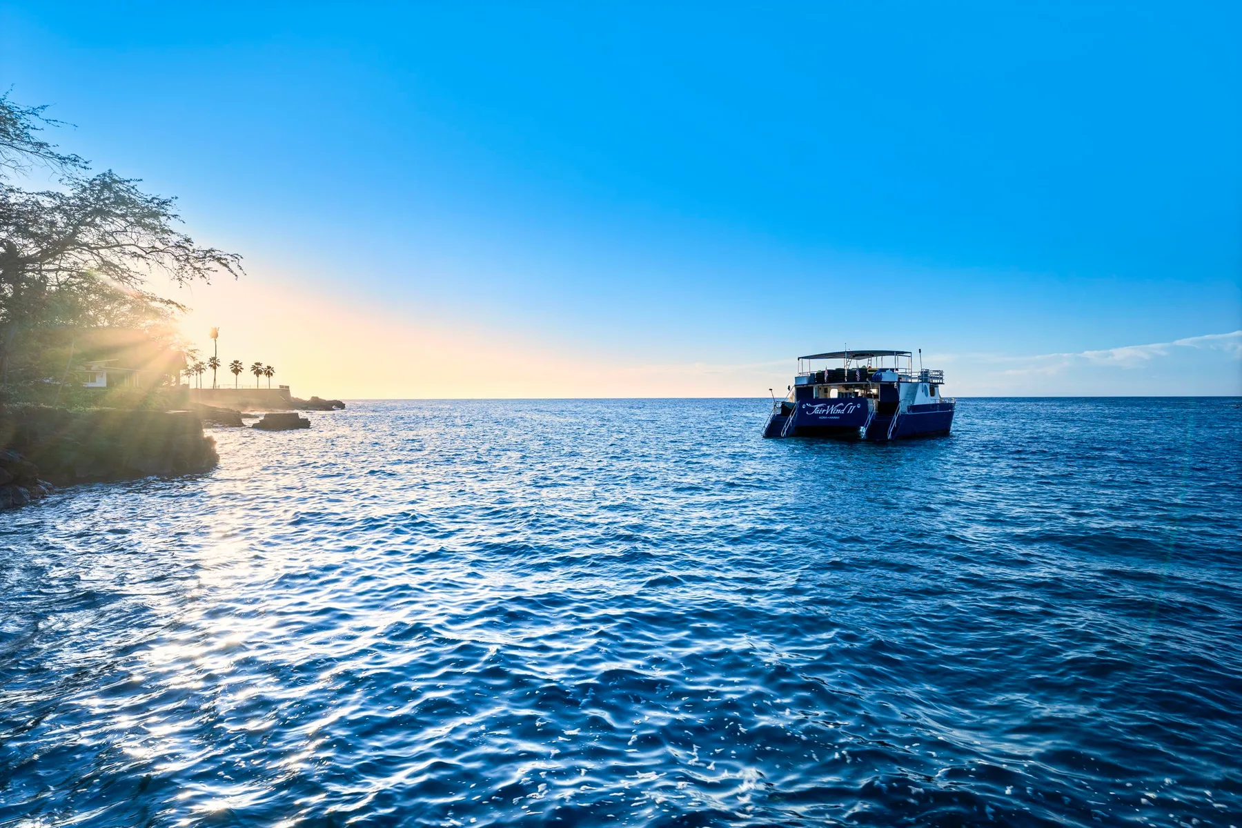 A boat floats on the sea near a rocky shoreline at sunset.