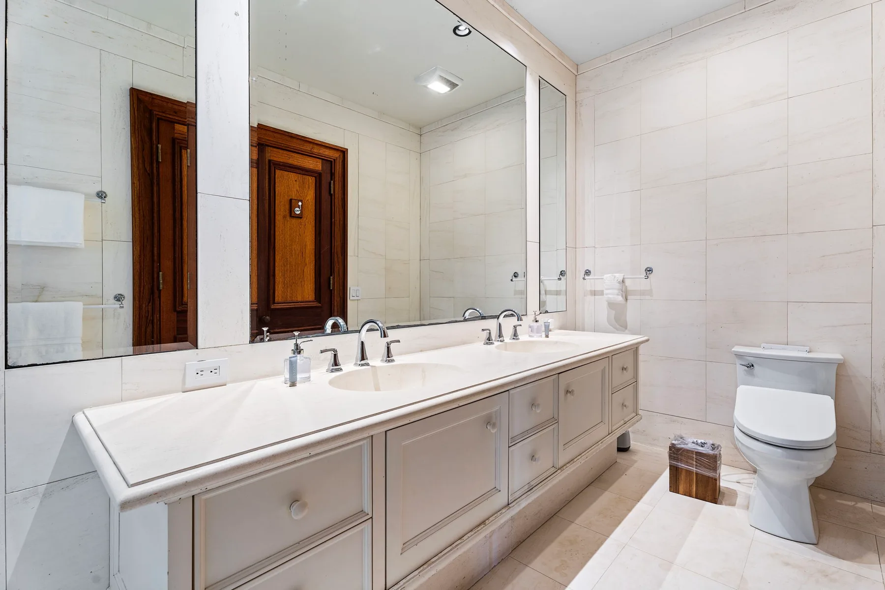 A bright bathroom with a long vanity and a large wall mirror.