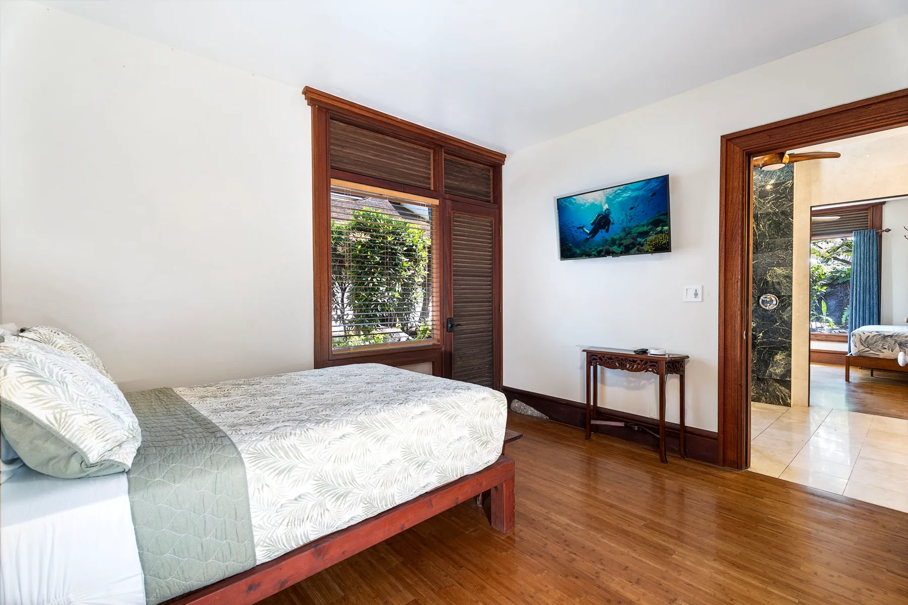 A bedroom with a bed, a wall-mounted television, and a wooden floor.