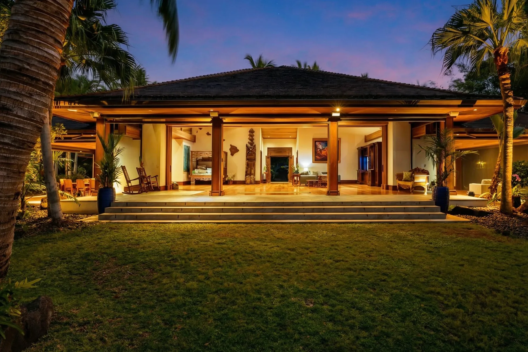 A warmly lit open-air house faces a lawn beneath the evening sky.